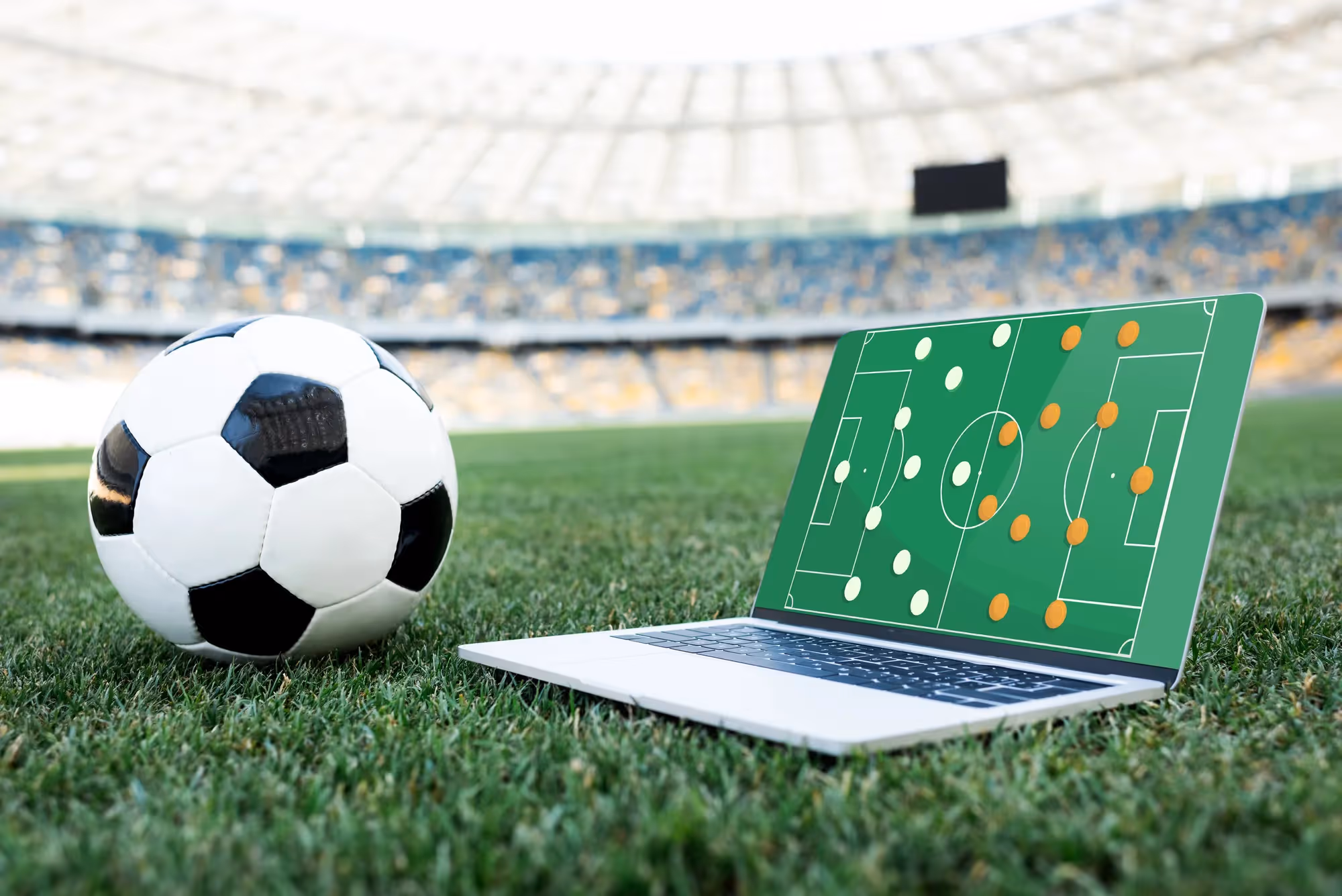 A soccer ball and a laptop computer with a soccer field on the screen.