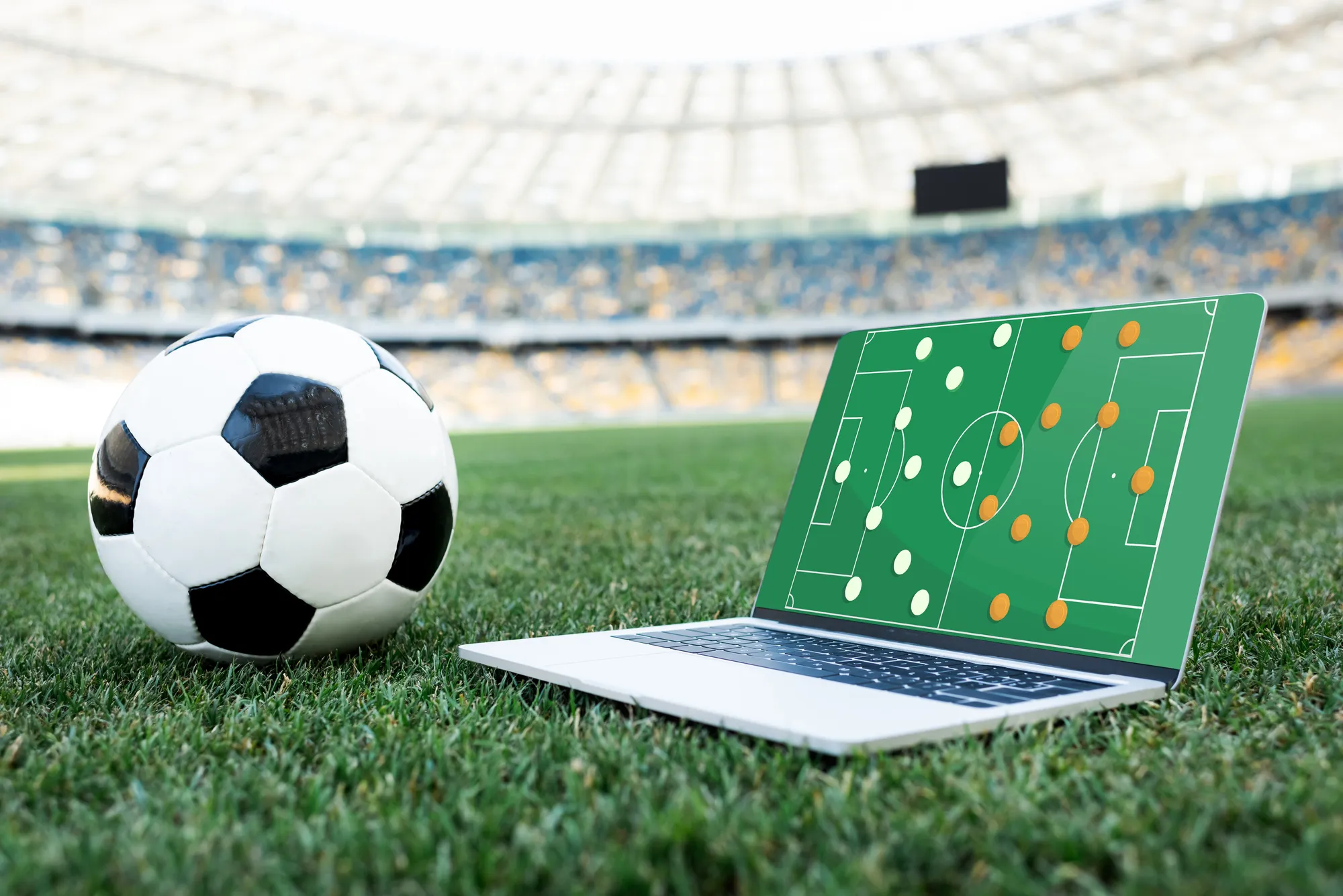 A soccer ball and a laptop computer with a soccer field on the screen.
