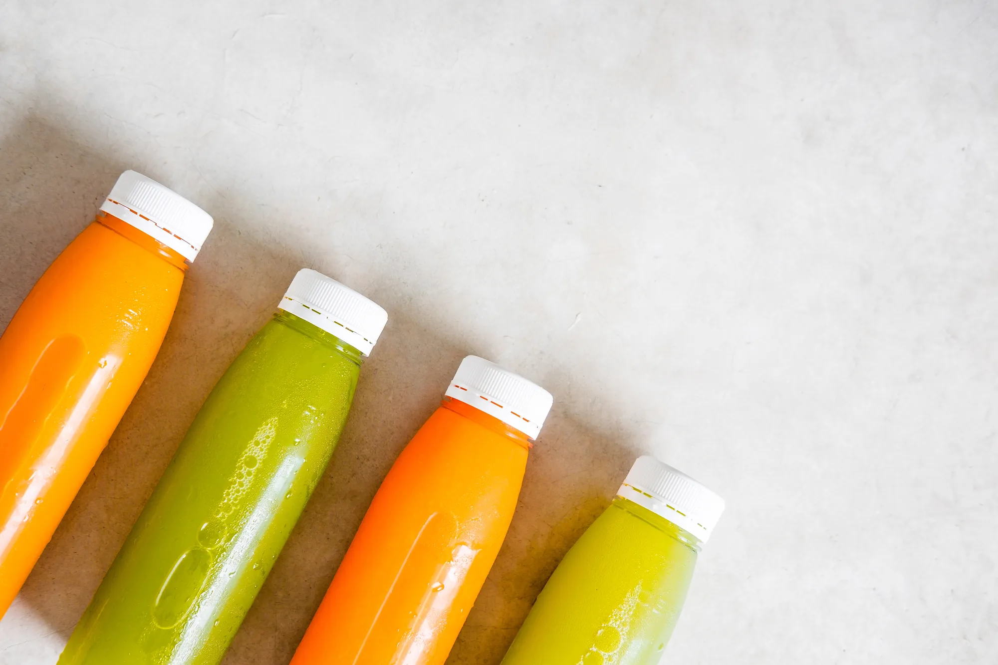 Four bottles of orange and green juice are lined up on a counter.