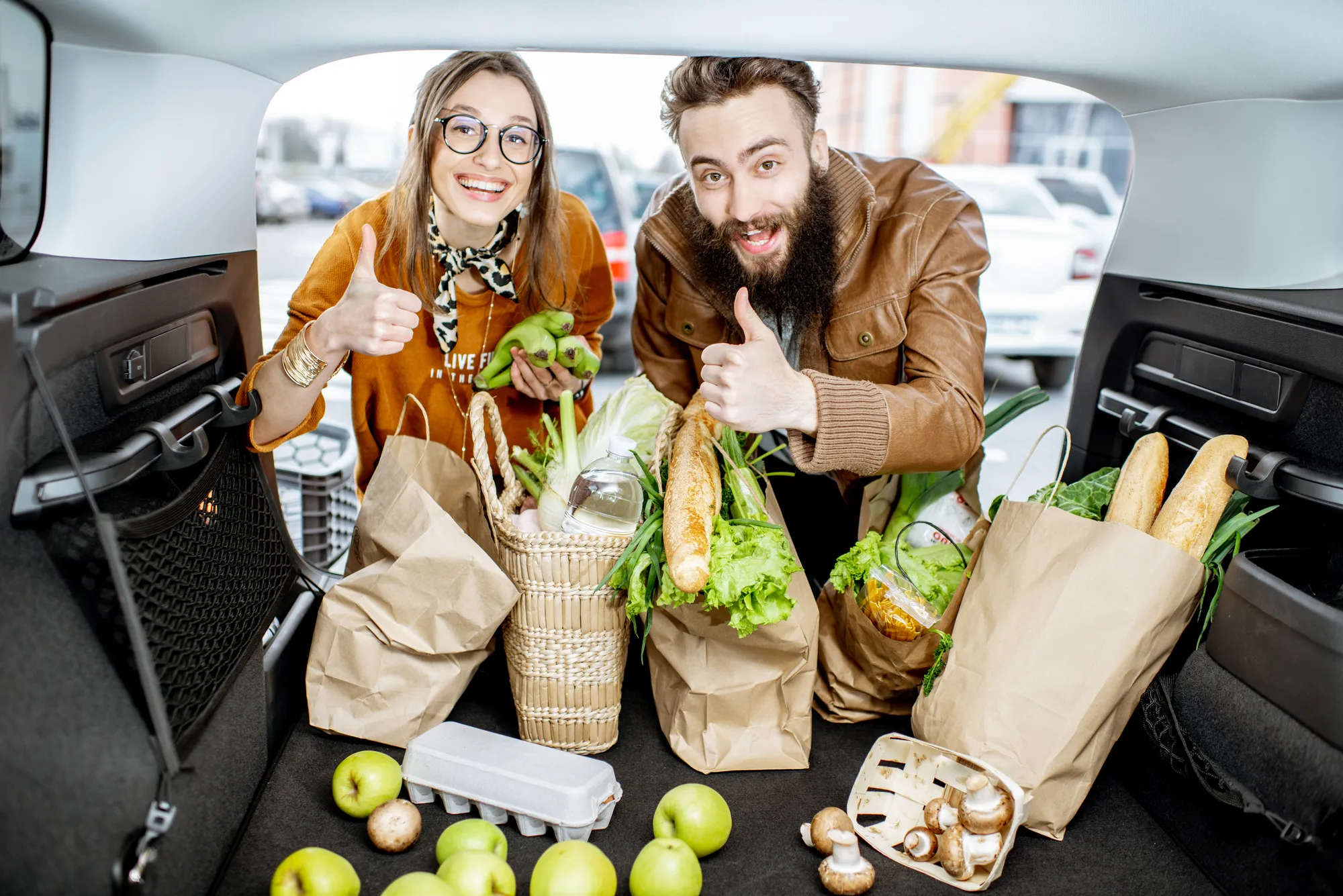 A man and woman are holding bags of produce in a car.