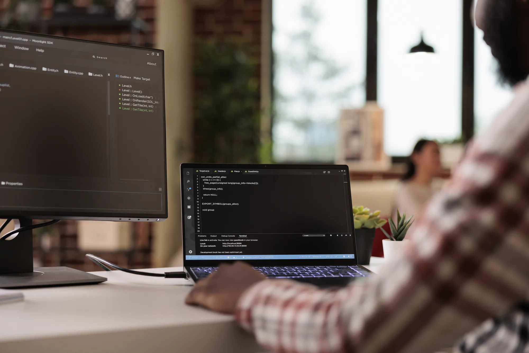 A man is working on a laptop in front of a large monitor.