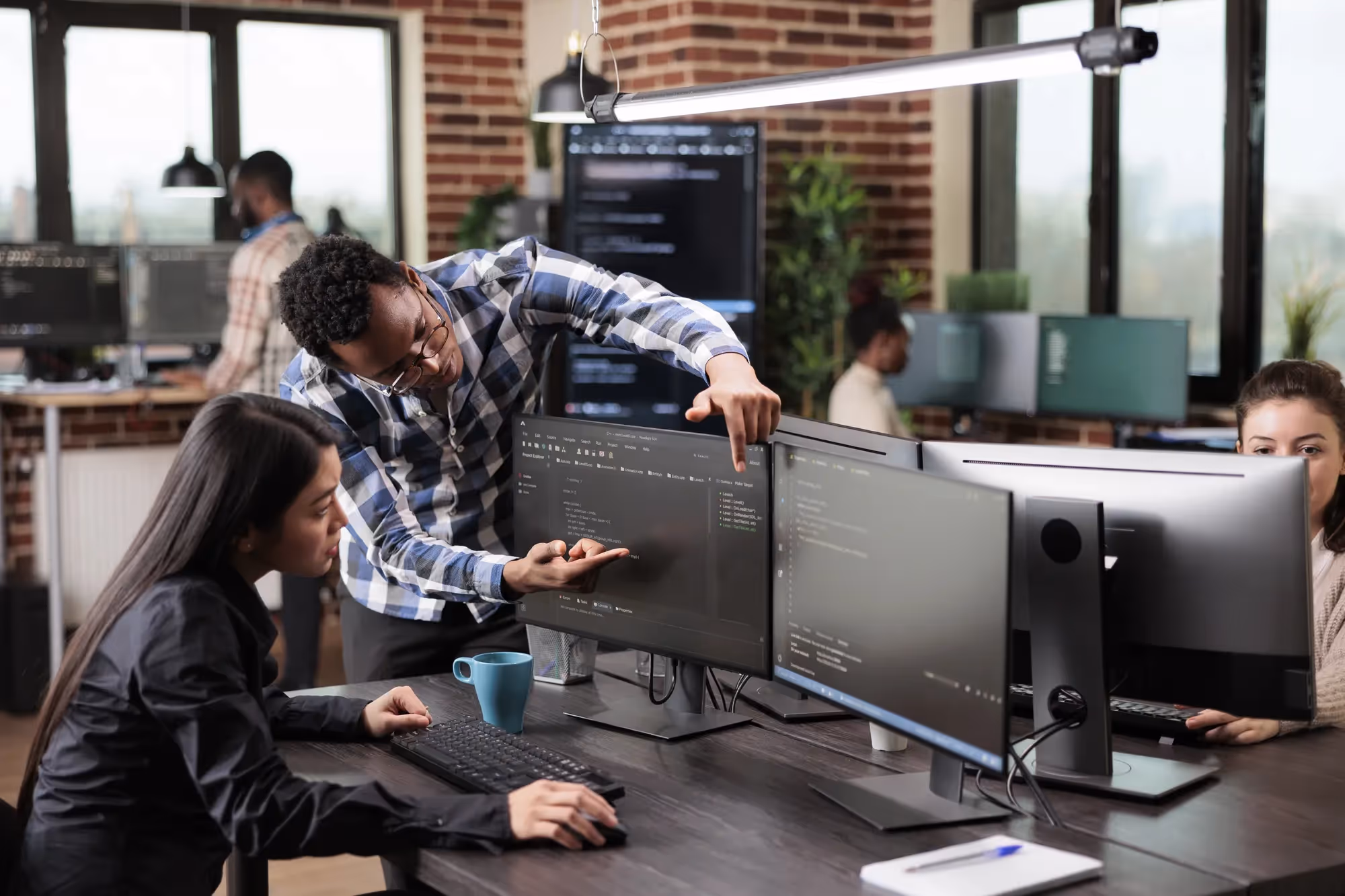 A man pointing at a computer screen with a woman sitting in front of it.