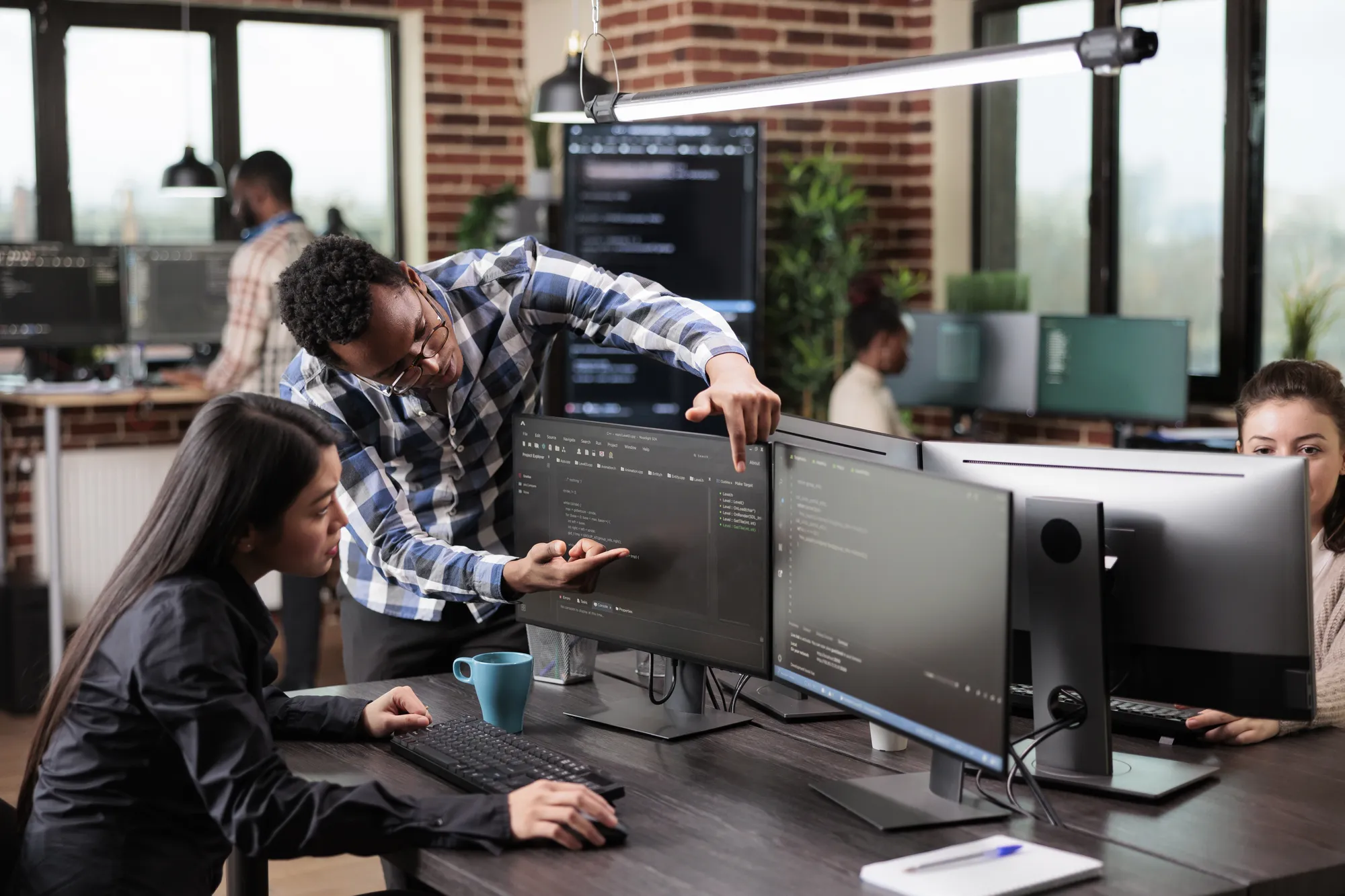 A man pointing at a computer screen with a woman sitting in front of it.