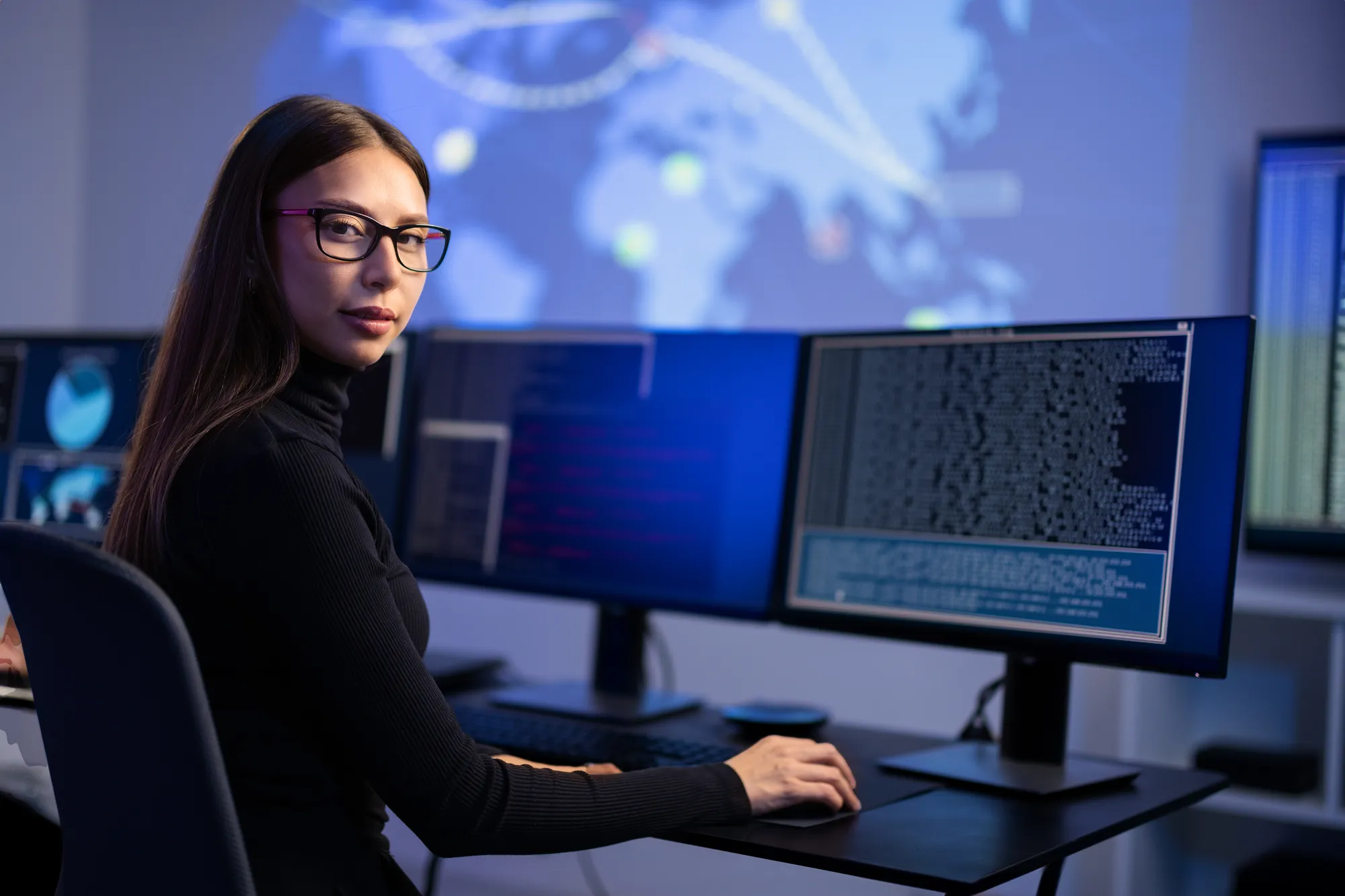 A woman wearing glasses and a black shirt is sitting in front of a computer.