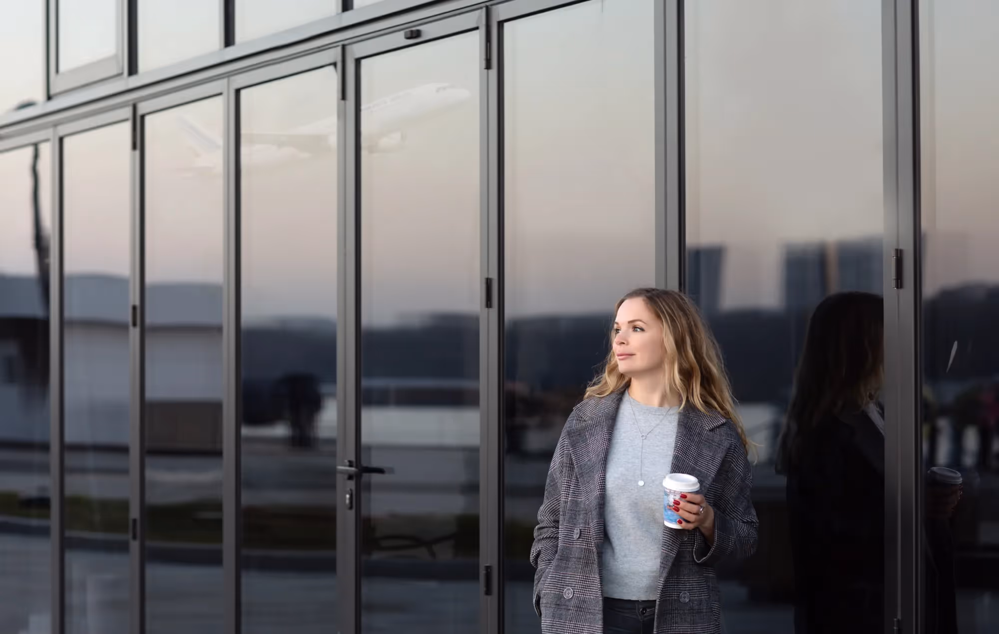 A woman with a coffee in her hand standing in front of a building.