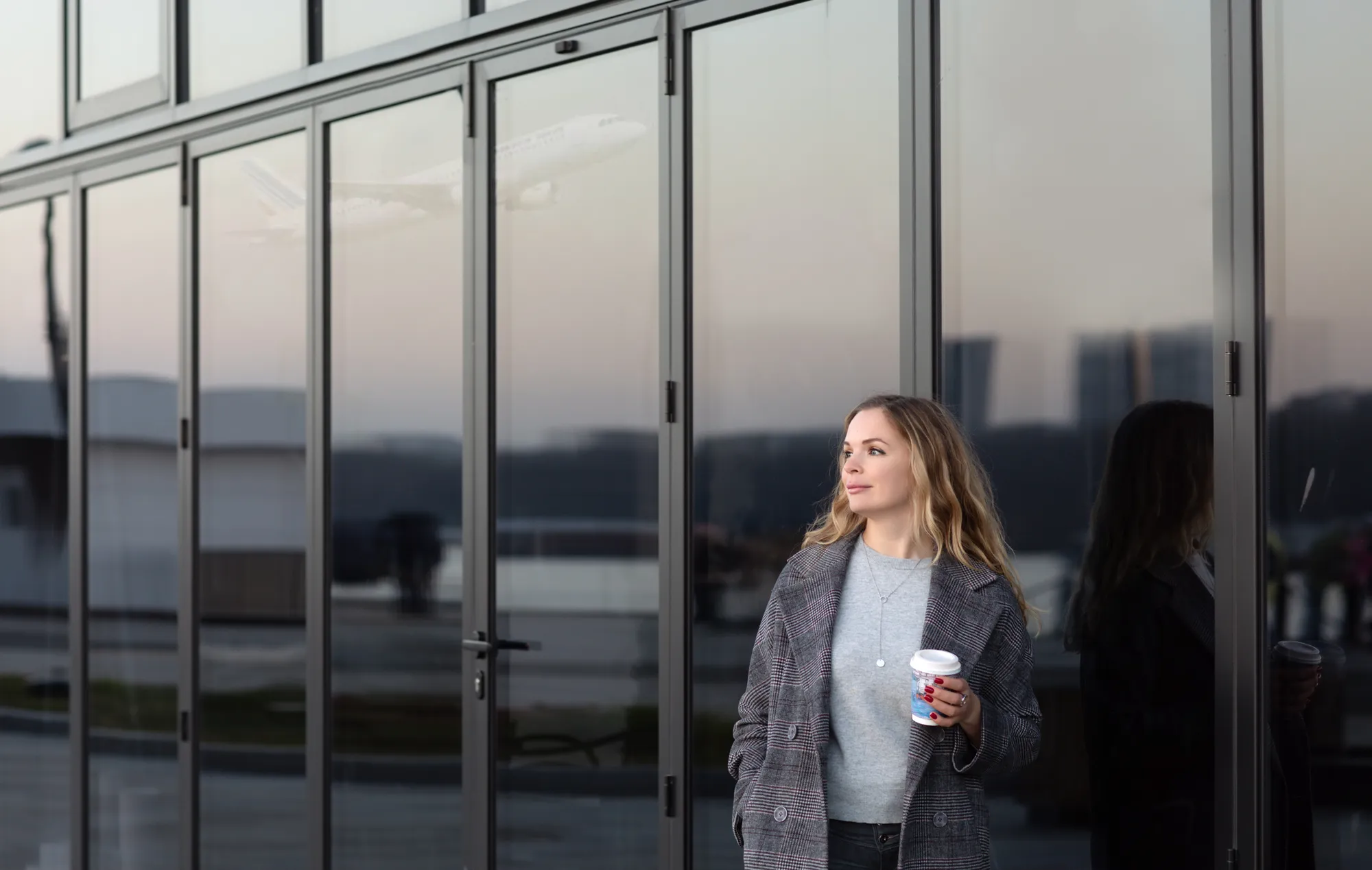 A woman with a coffee in her hand standing in front of a building.