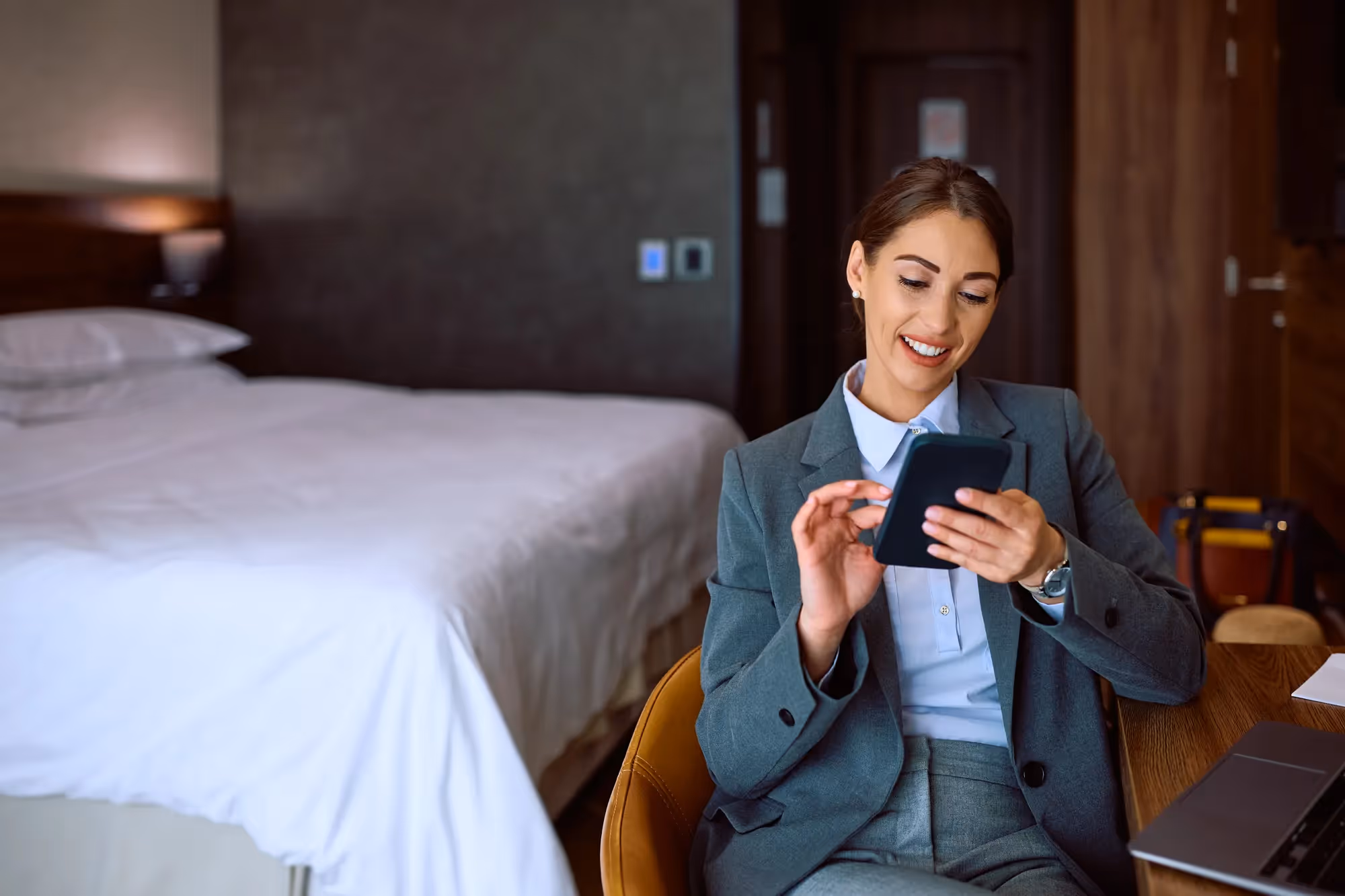 A woman in a grey suit is sitting in a chair and looking at a tablet.