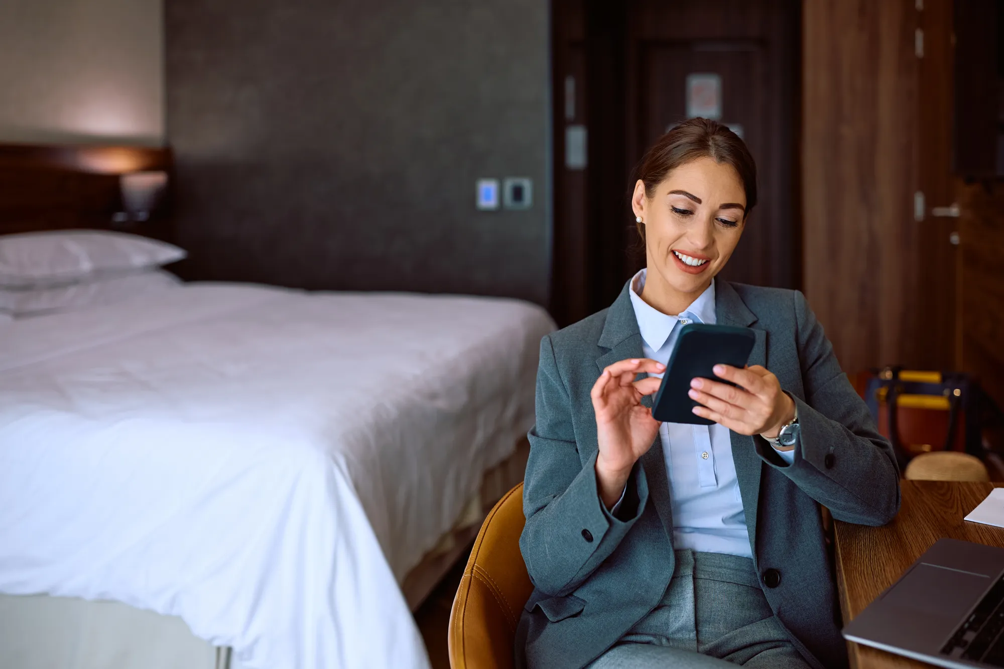 A woman in a grey suit is sitting in a chair and looking at a tablet.