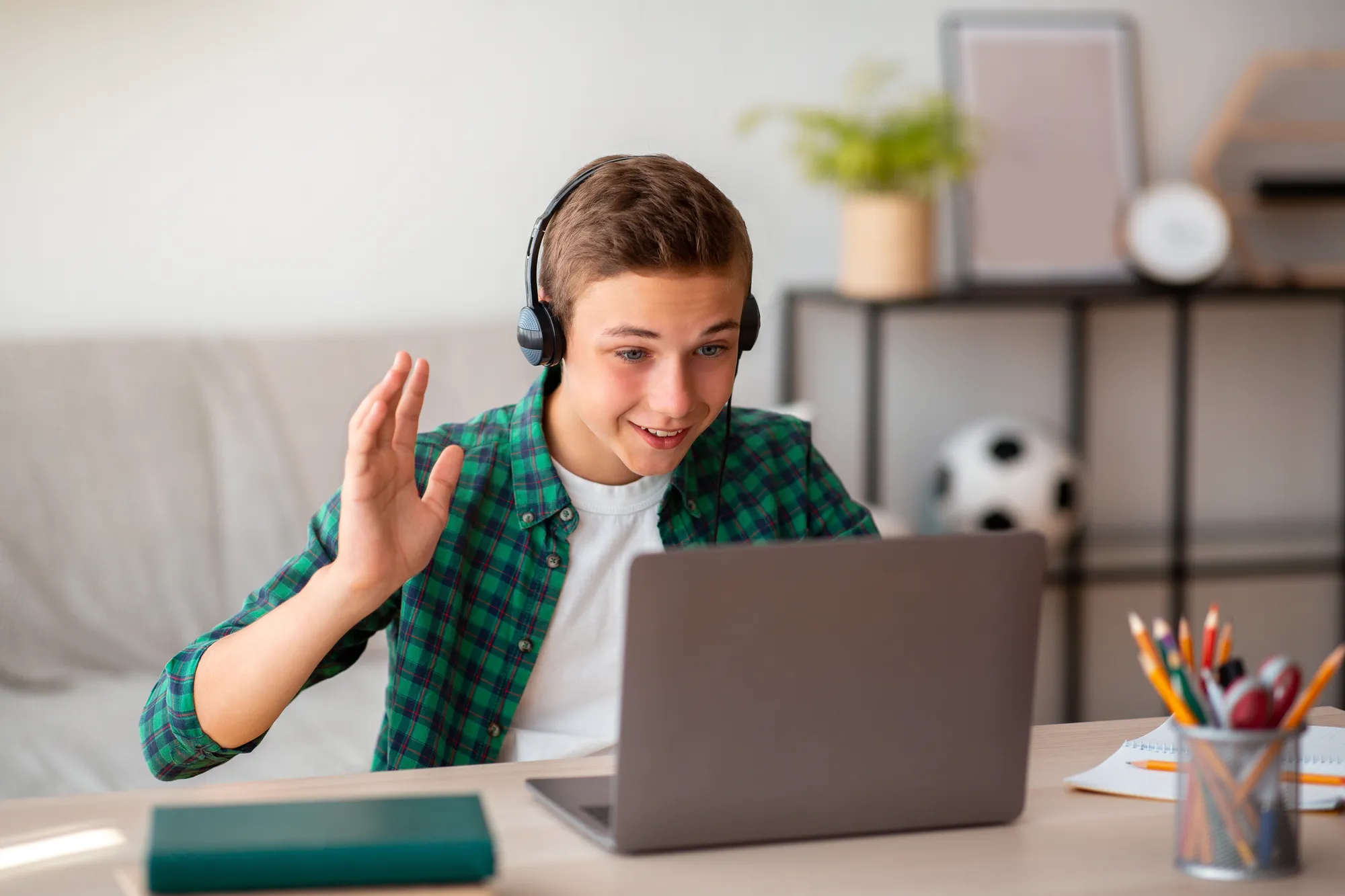 A young man wearing headphones and a plaid shirt is using a laptop.