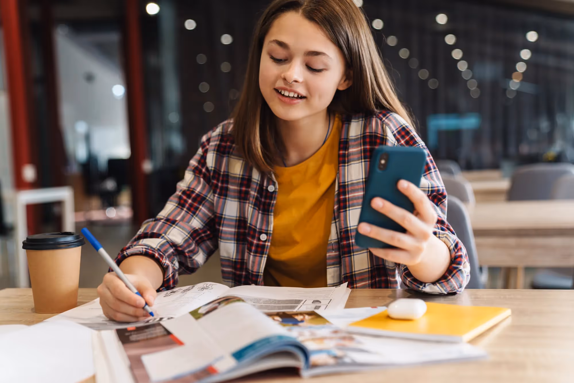 A woman is sitting at a table with a magazine and a cell phone.