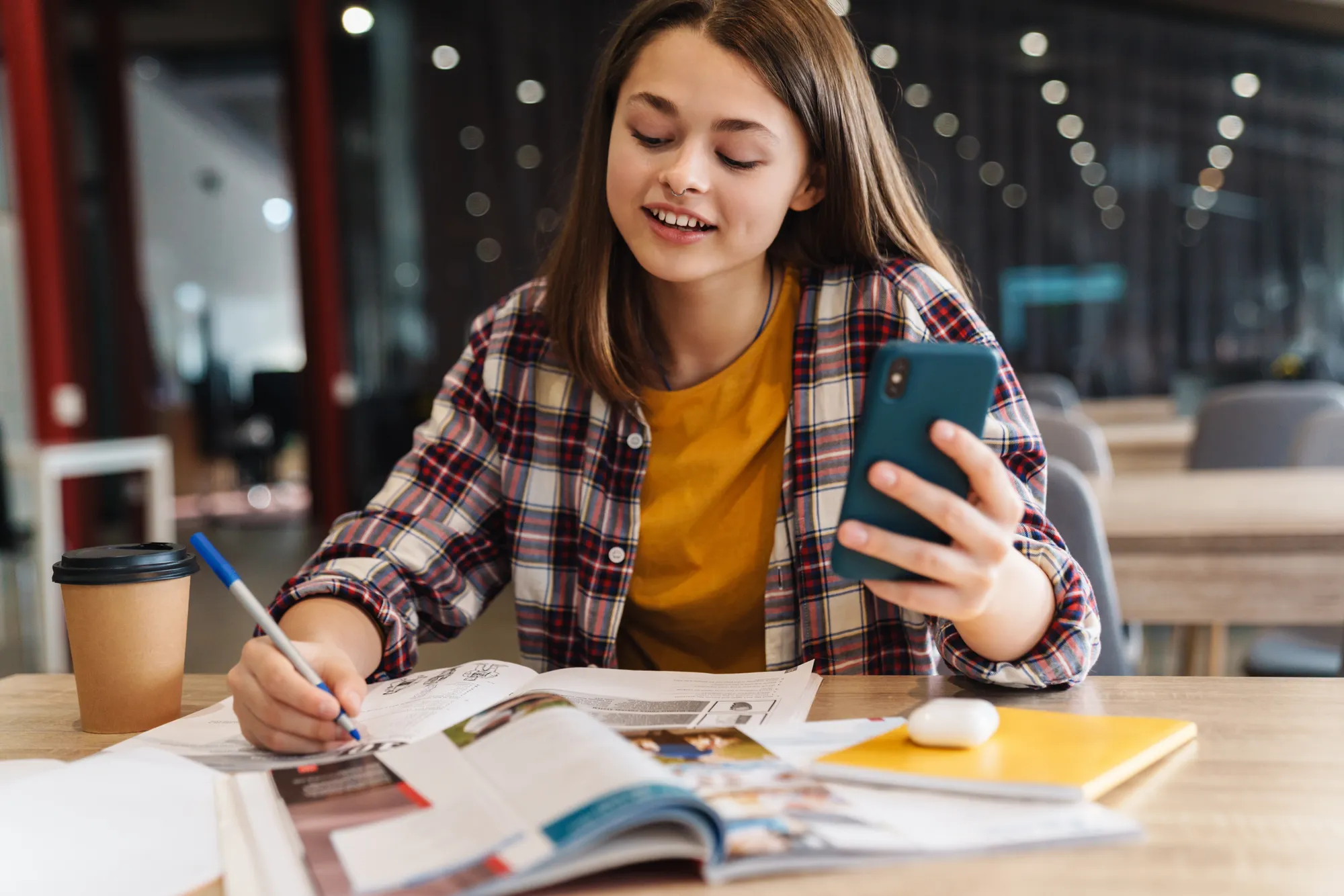 A woman is sitting at a table with a magazine and a cell phone.