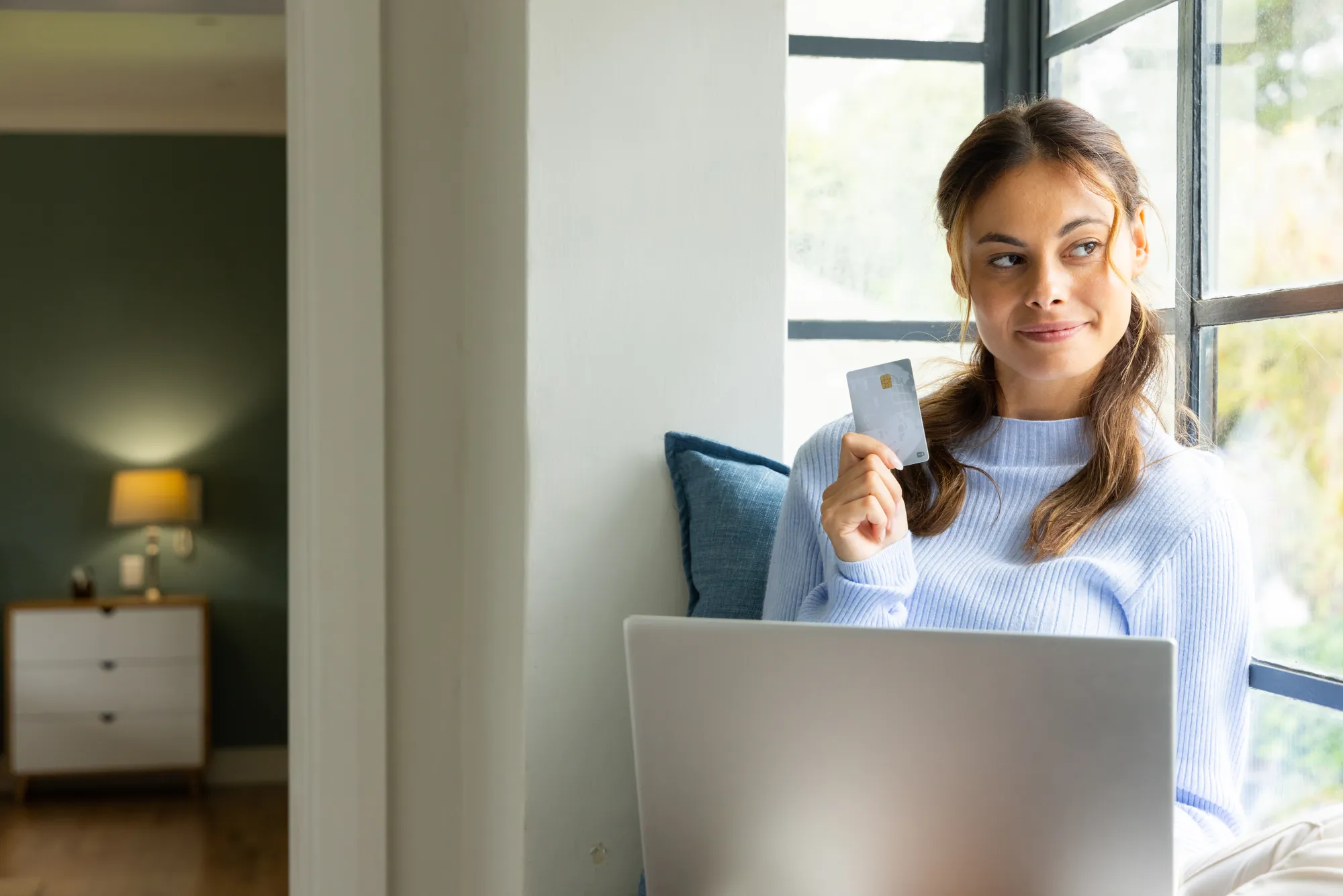 A woman sitting in front of a laptop holding a card.