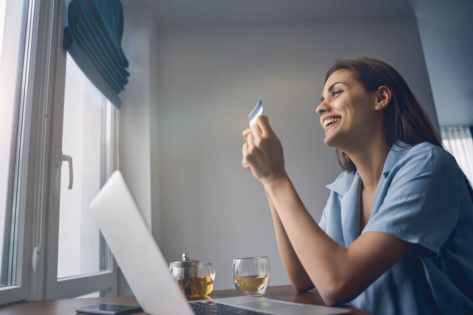 A woman holding a card in front of a laptop.