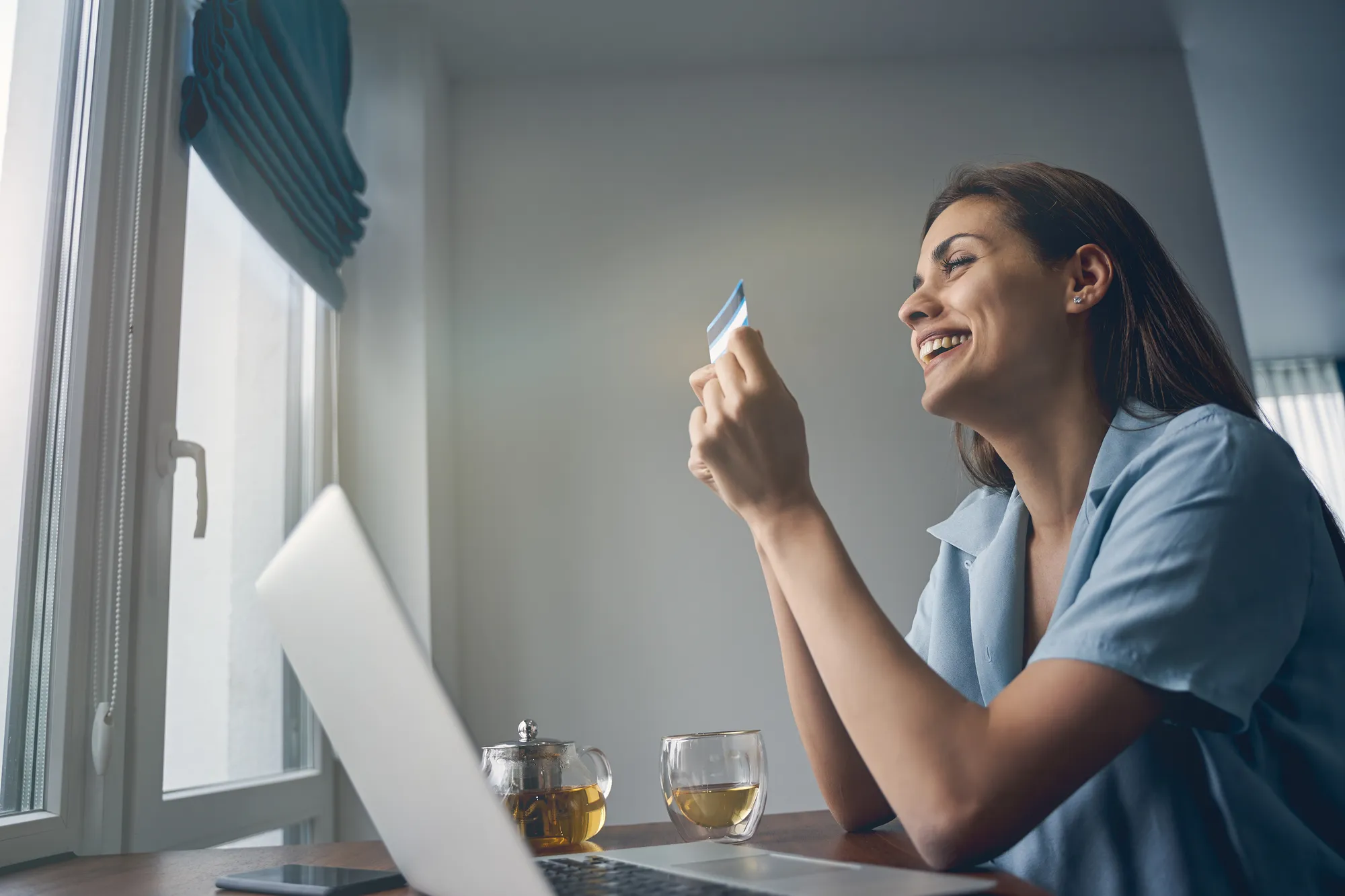 A woman holding a card in front of a laptop.