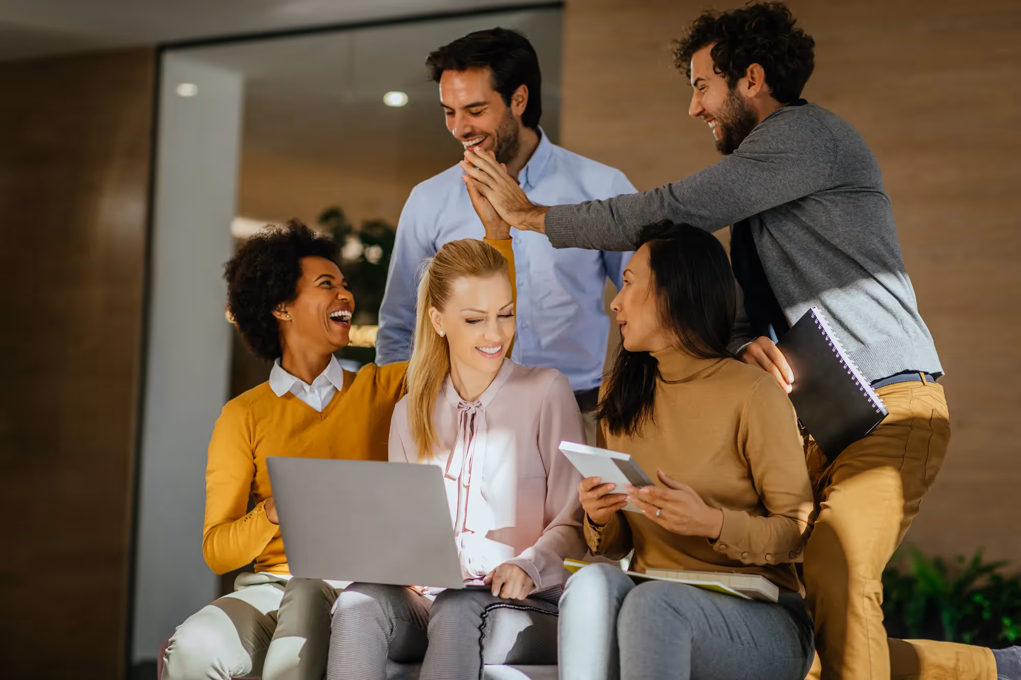 A group of people sitting together and smiling while one of them is using a laptop.