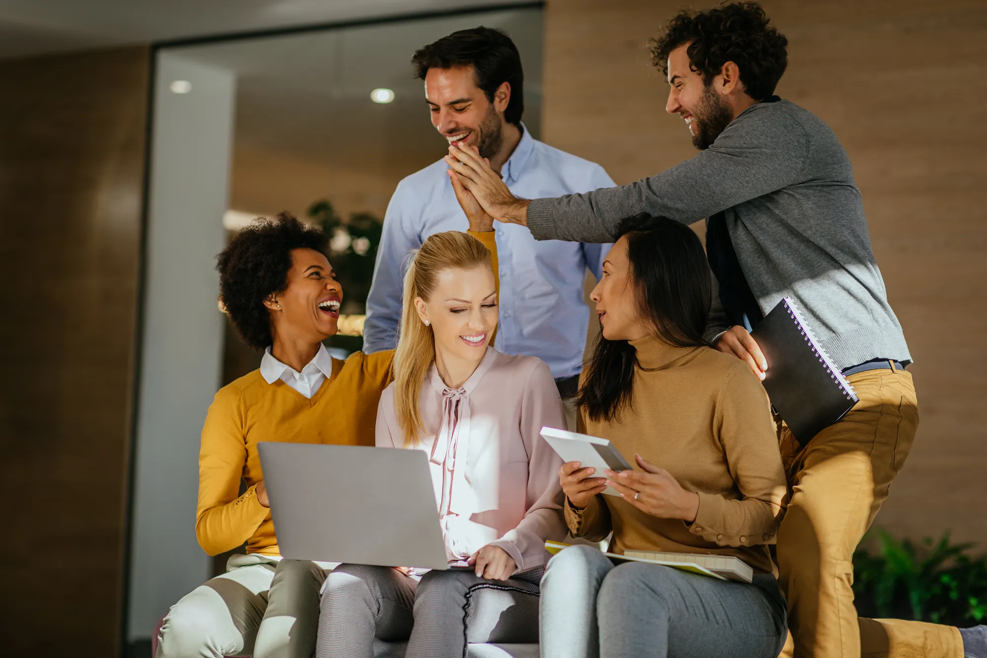 A group of people sitting together and smiling while one of them is using a laptop.