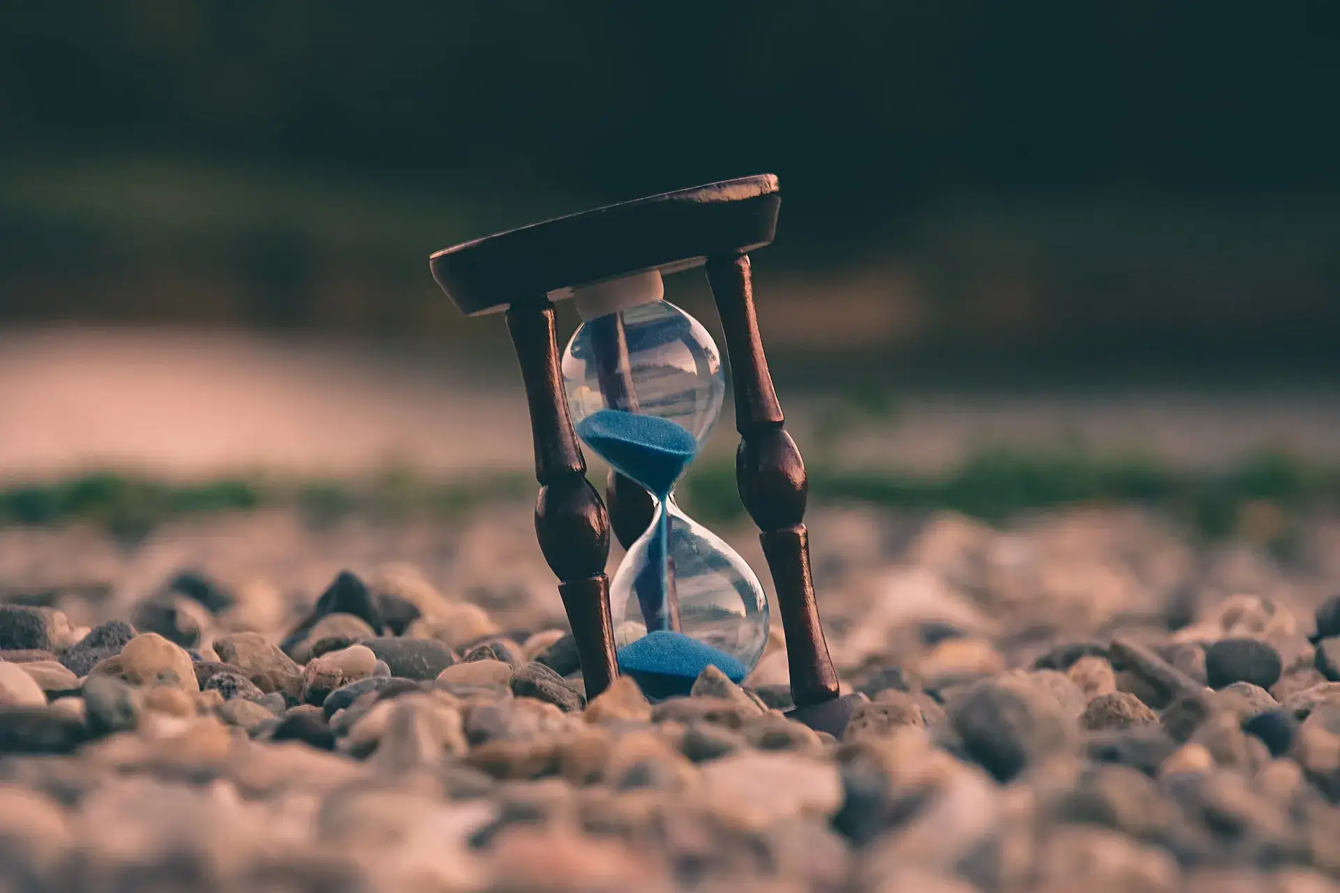 A wooden clock with a blue face and a rock on the ground.