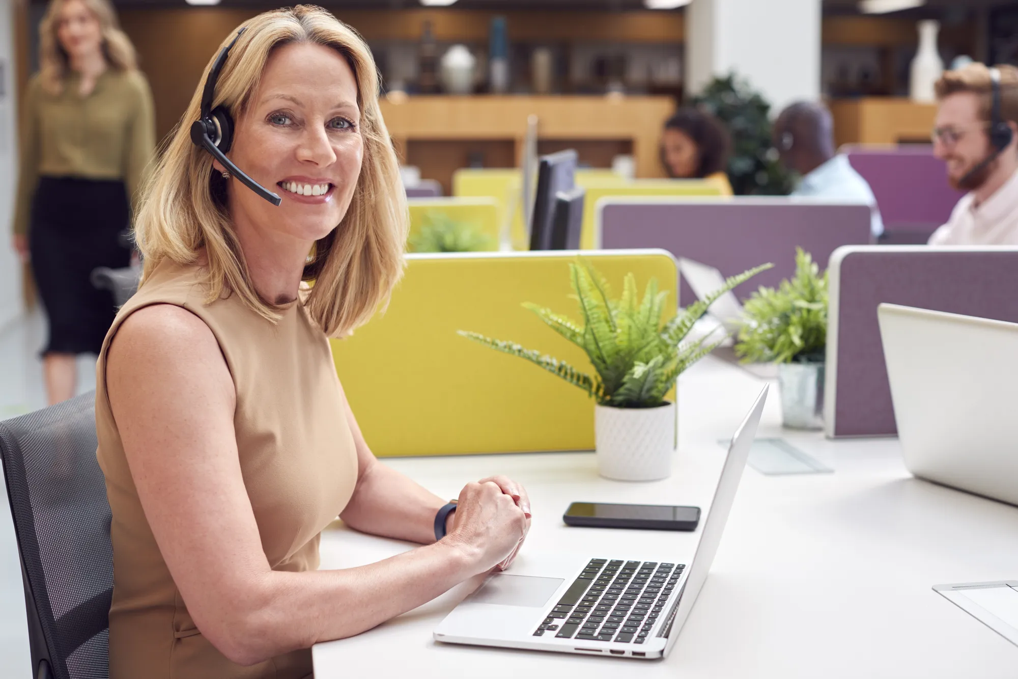 A woman wearing a headset and smiling while working on a laptop.