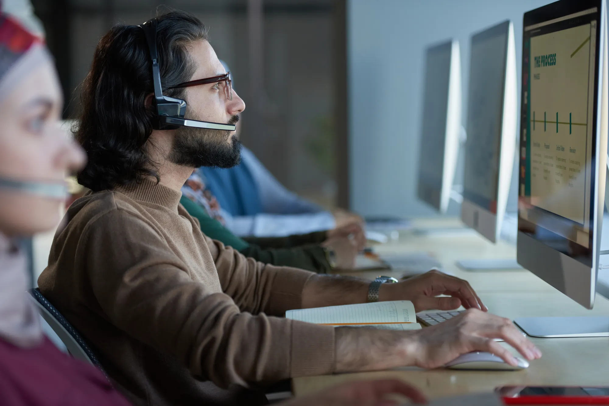 A man wearing glasses and a headset is typing on a computer.
