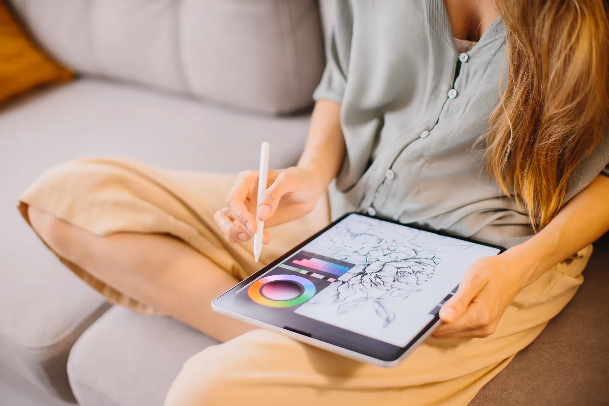 A woman is sitting on a couch and drawing on a tablet.