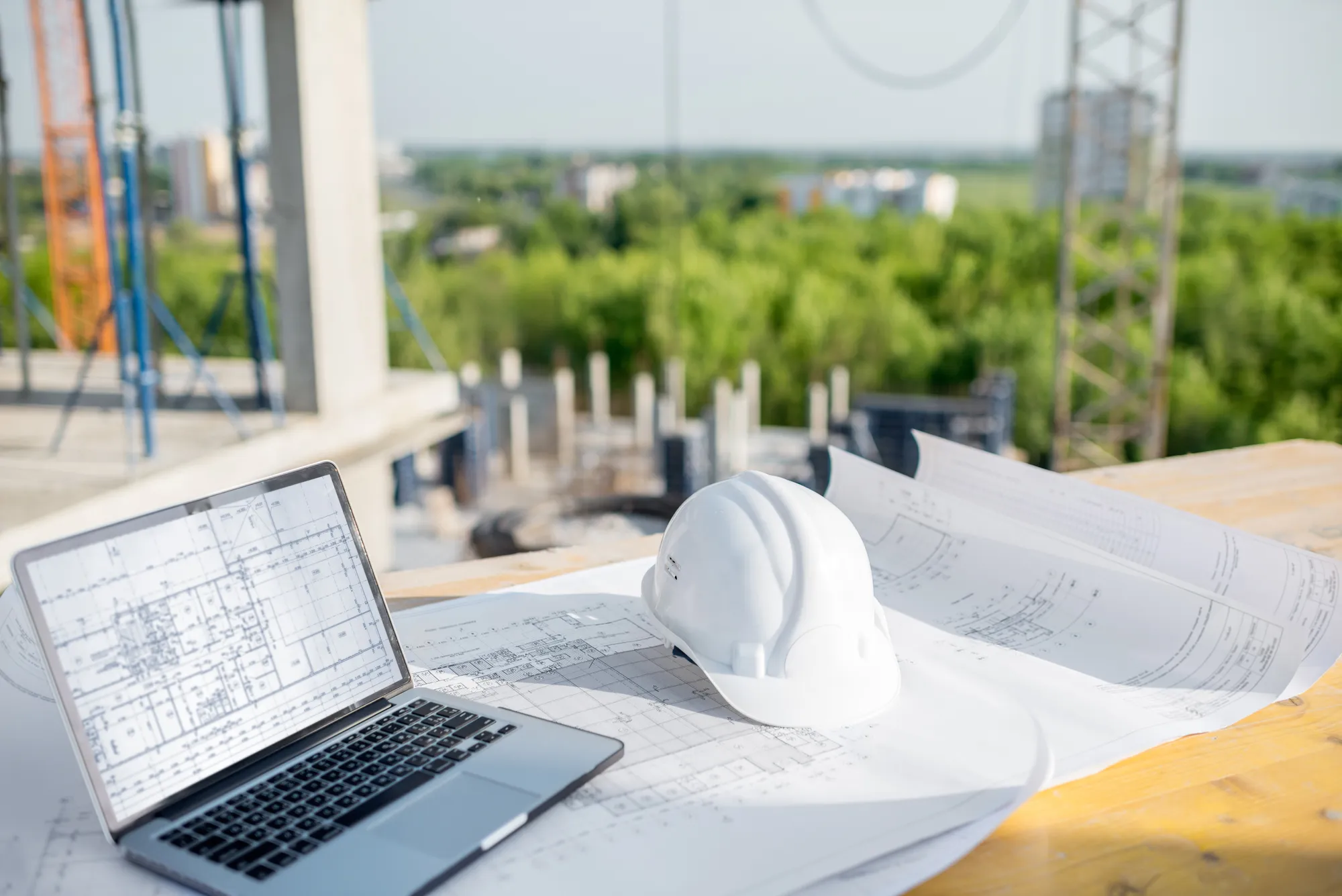 A laptop with a white hard hat on top of a blueprint.