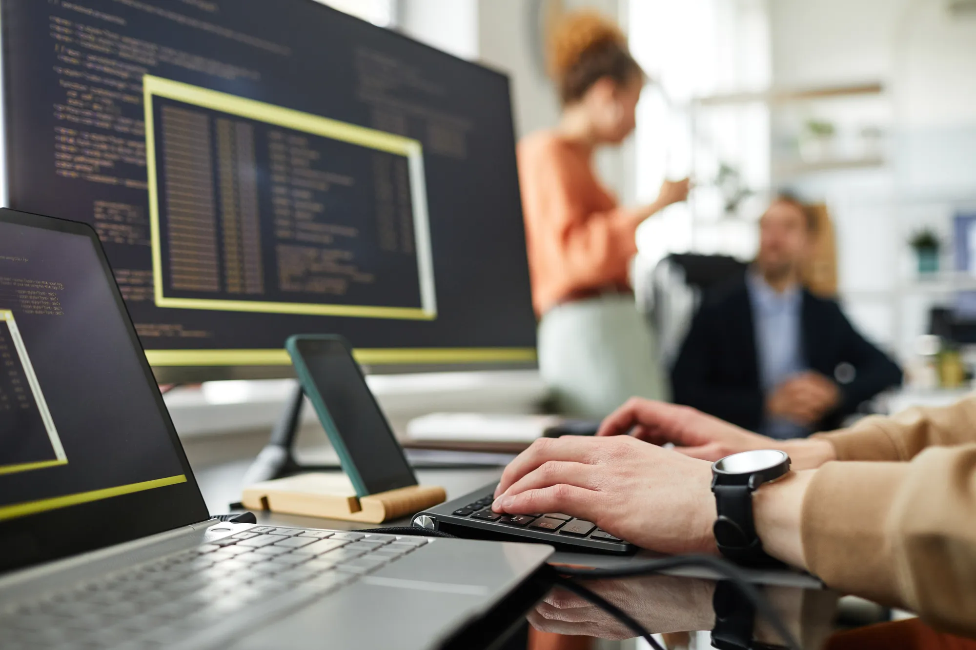 A person is typing on a laptop in front of a large monitor.