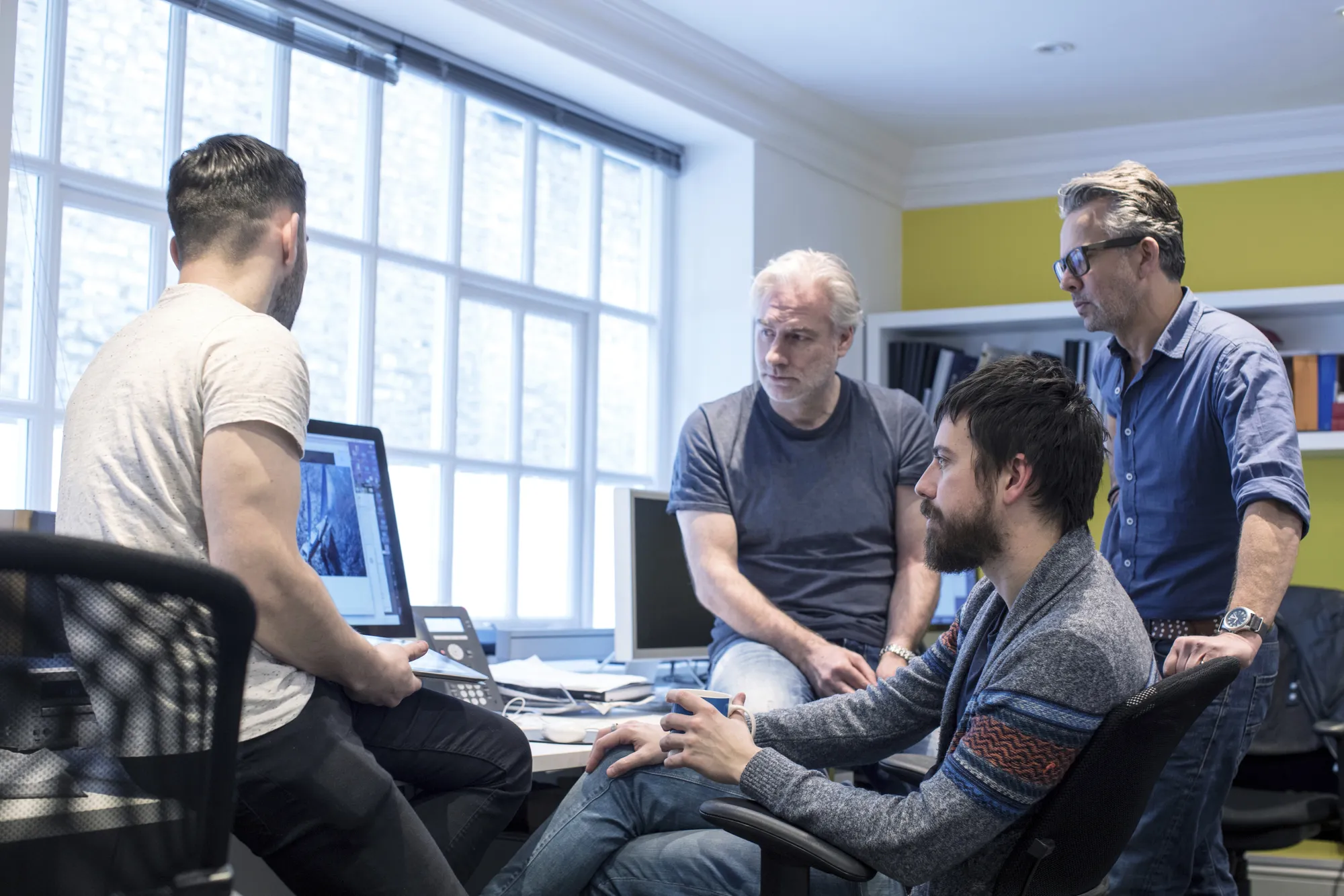 A group of men sitting around a table with a computer monitor.
