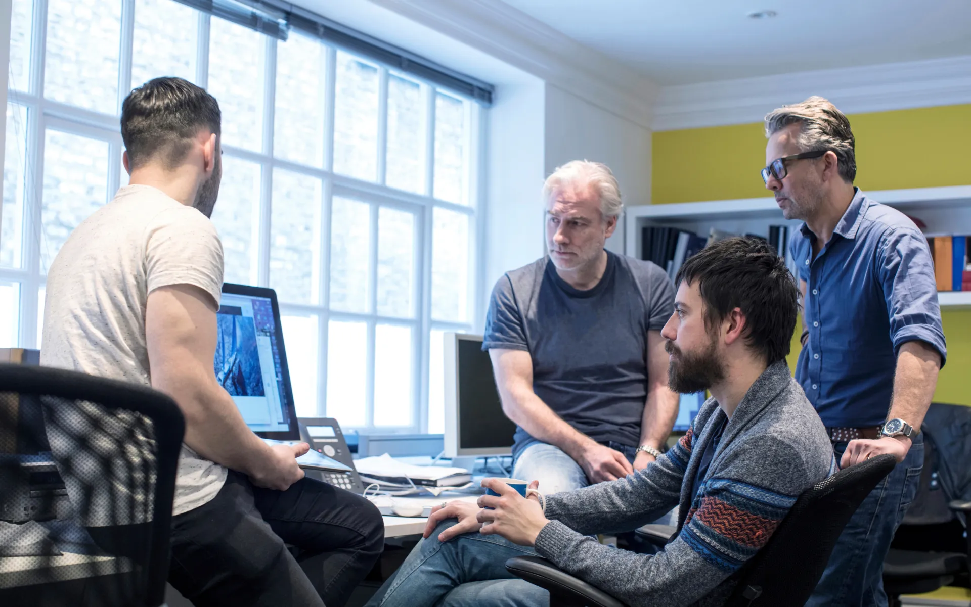A group of men sitting around a table with a laptop.