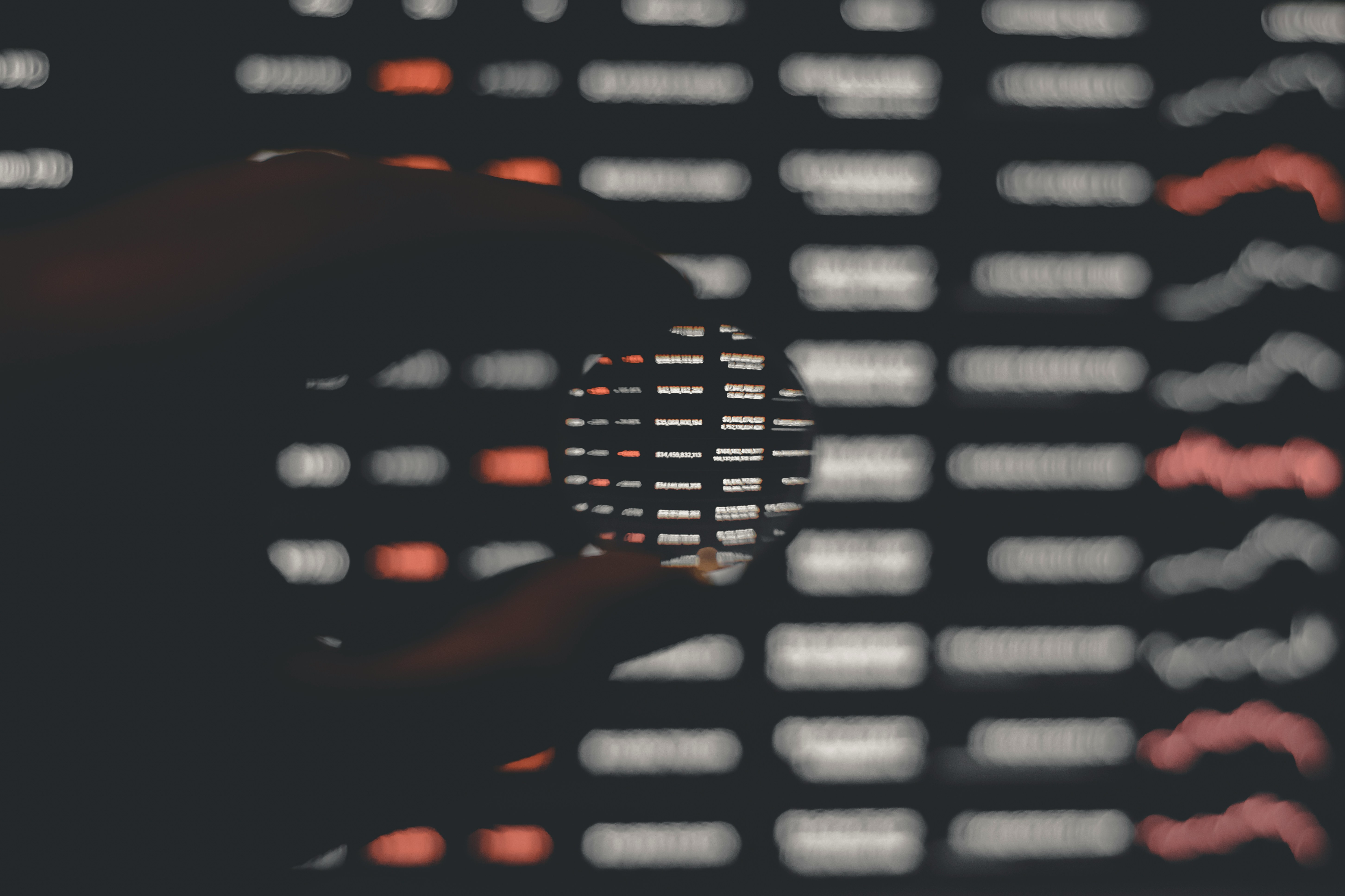 A hand holding a magnifying glass over a computer screen.