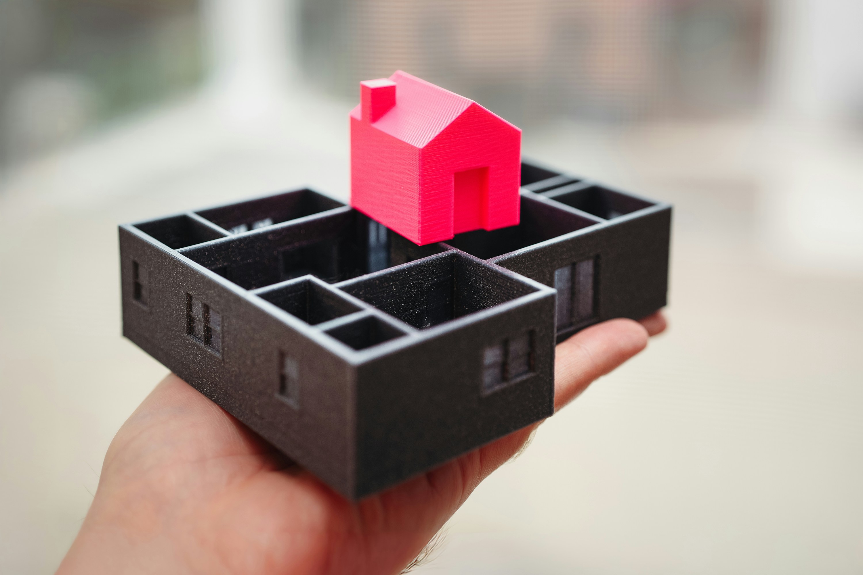 A hand holding a toy house with a red roof.