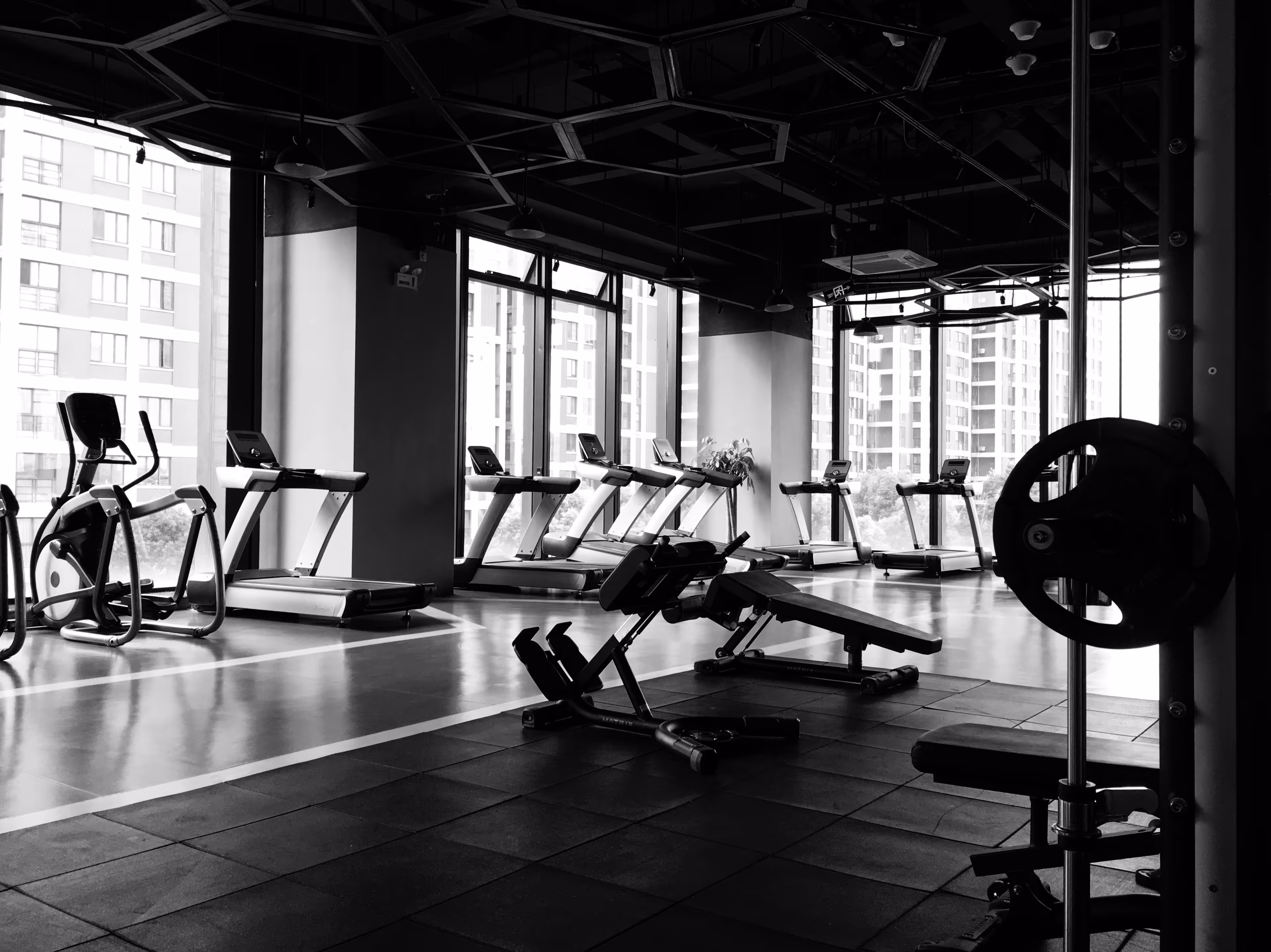 A black and white photo of a gym with a bench and a treadmill.