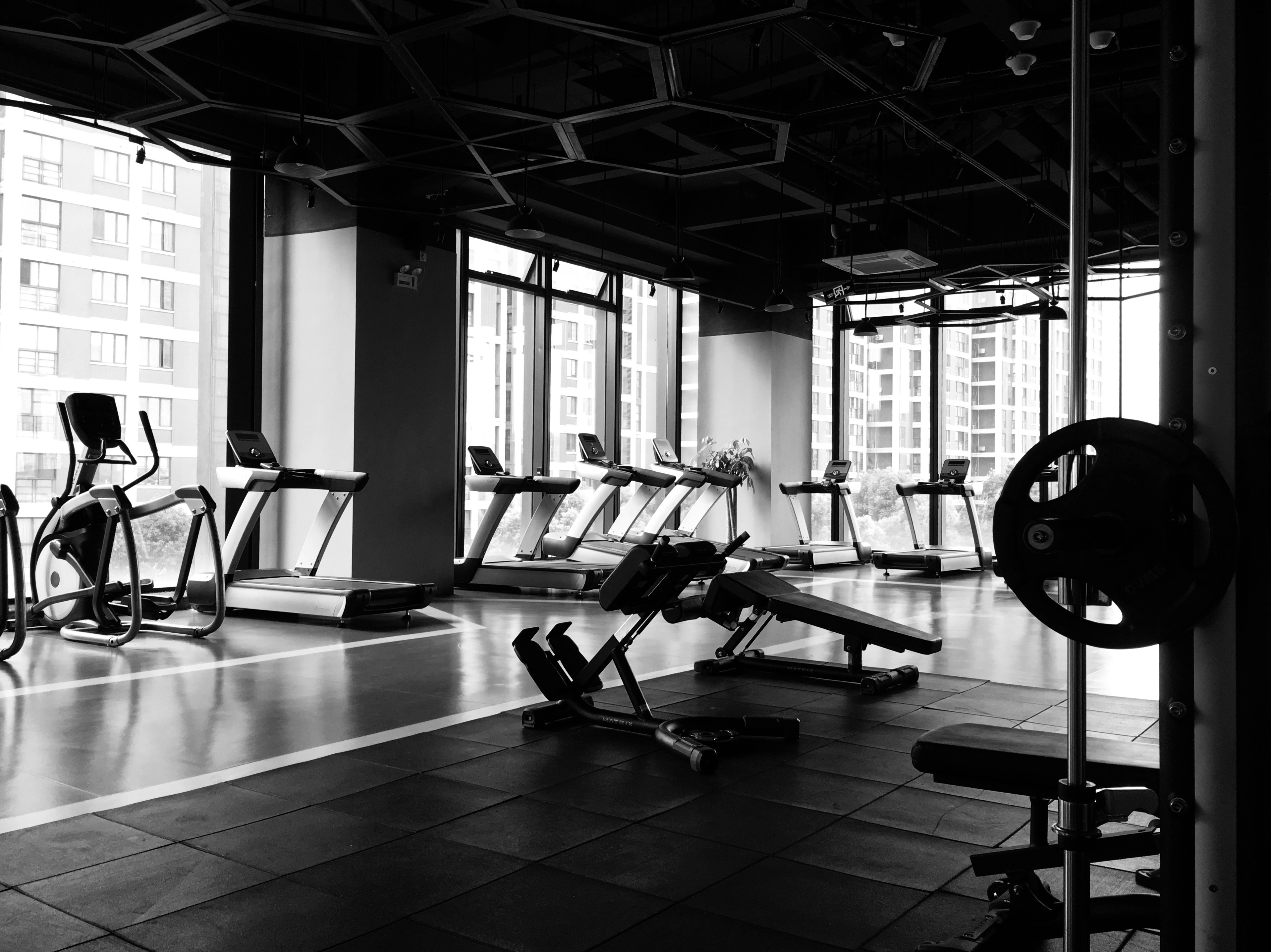 A black and white photo of a gym with a bench and a treadmill.