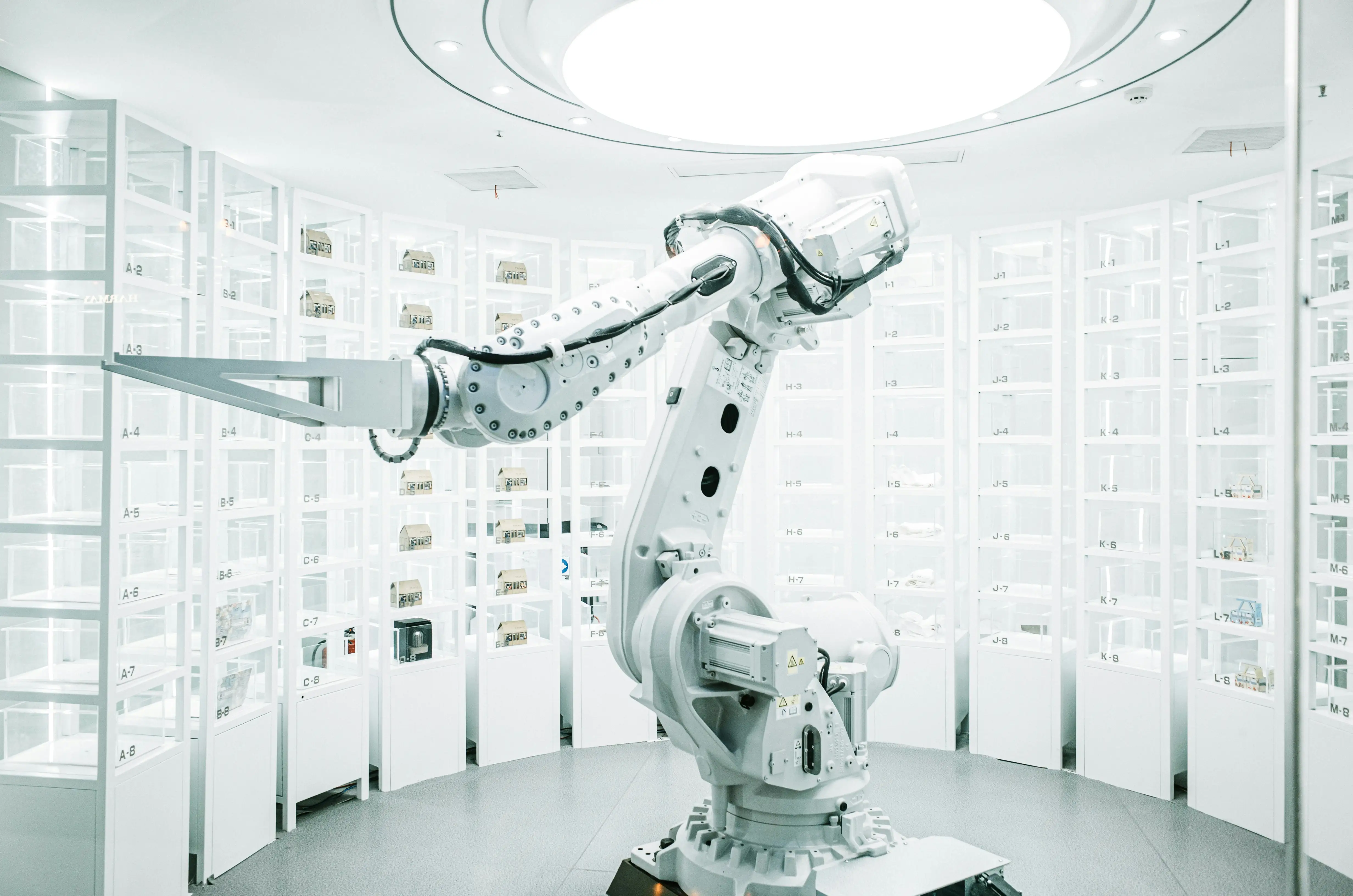 A robot is in a white room with a large light above it.