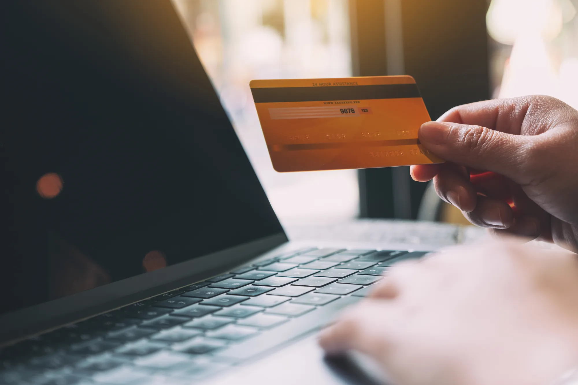 A person holding a credit card in front of a laptop.