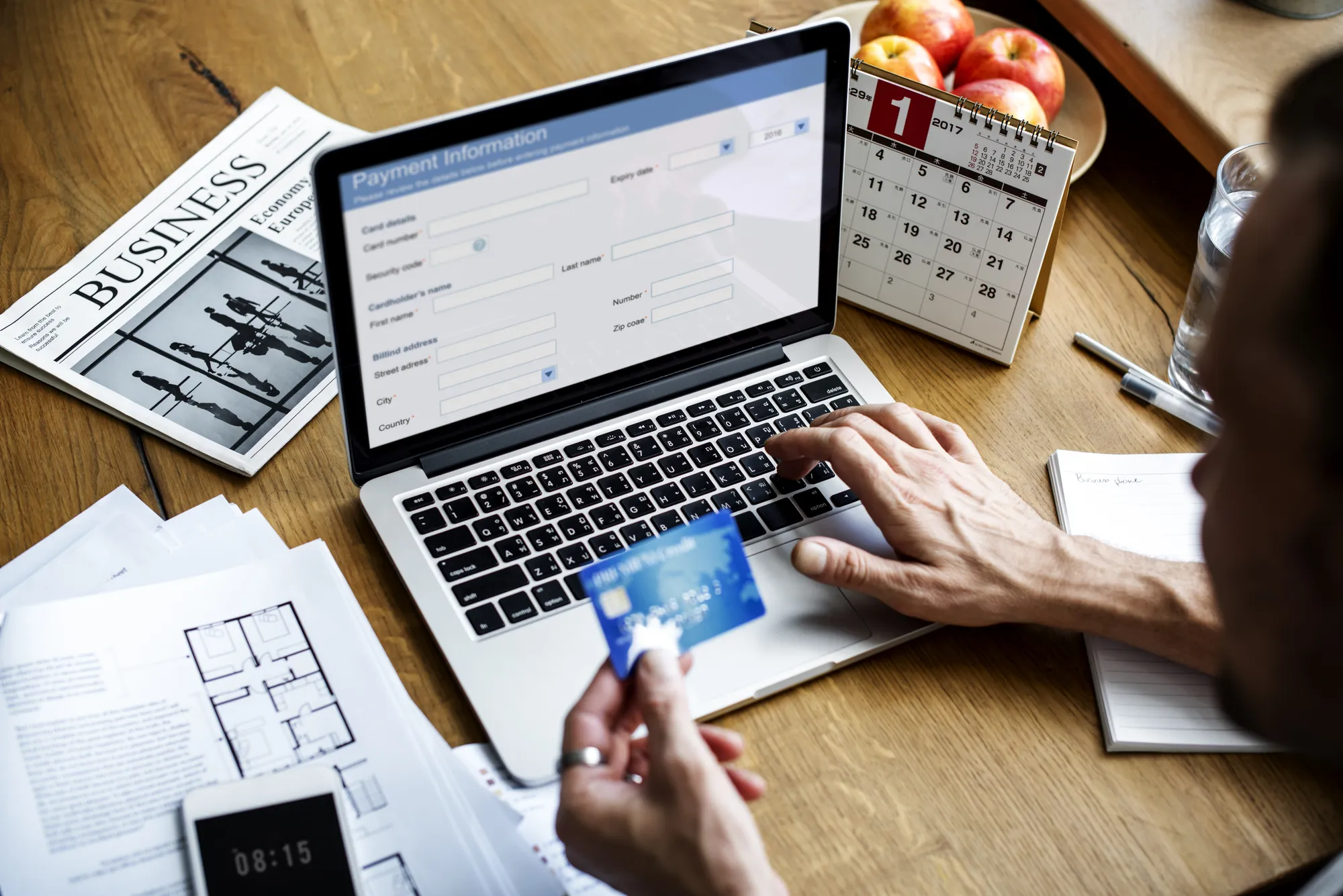 A person is typing on a laptop with a calendar and apples in the background.