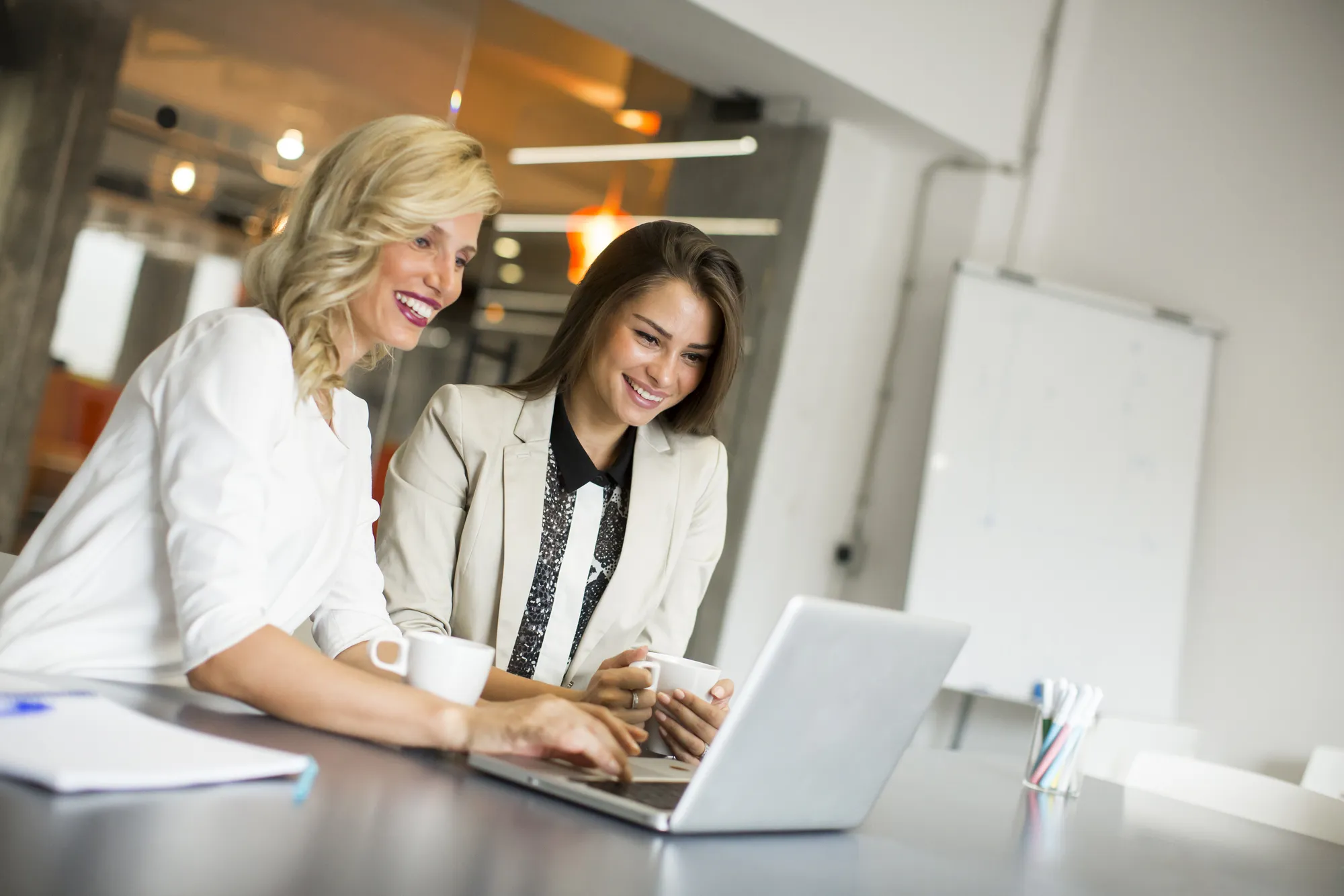Two women sitting at a desk using a laptop.
