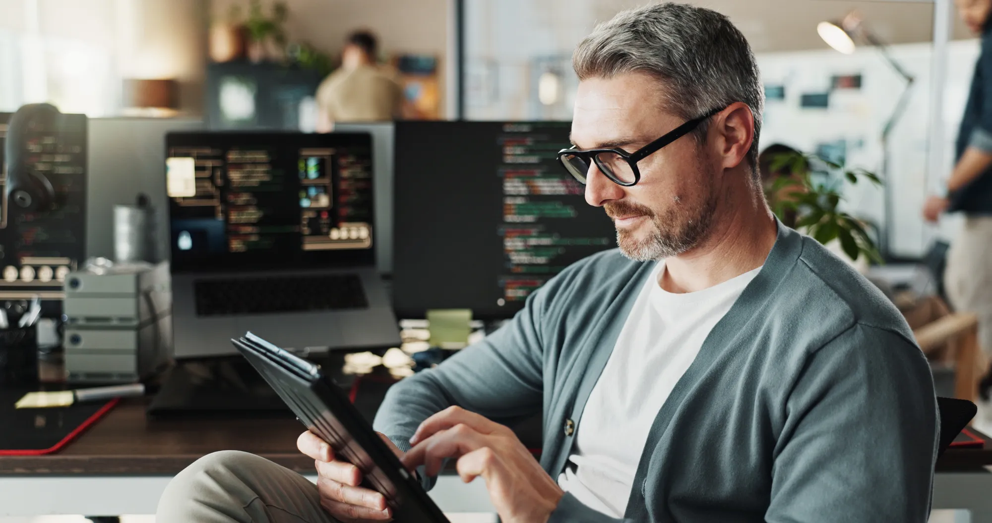 A man in a grey sweater is looking at a tablet.