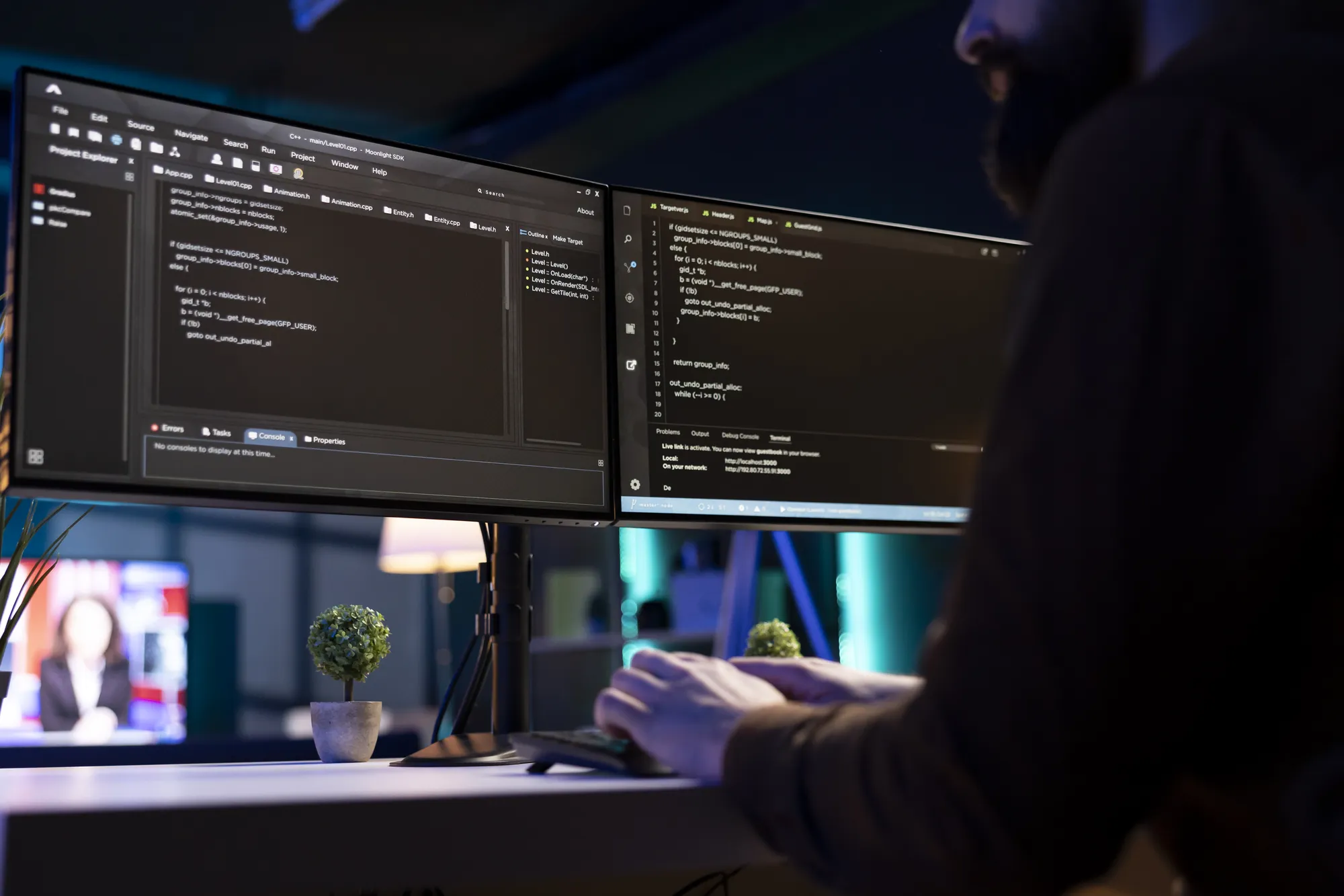 A man is typing on a computer with two large monitors in front of him.
