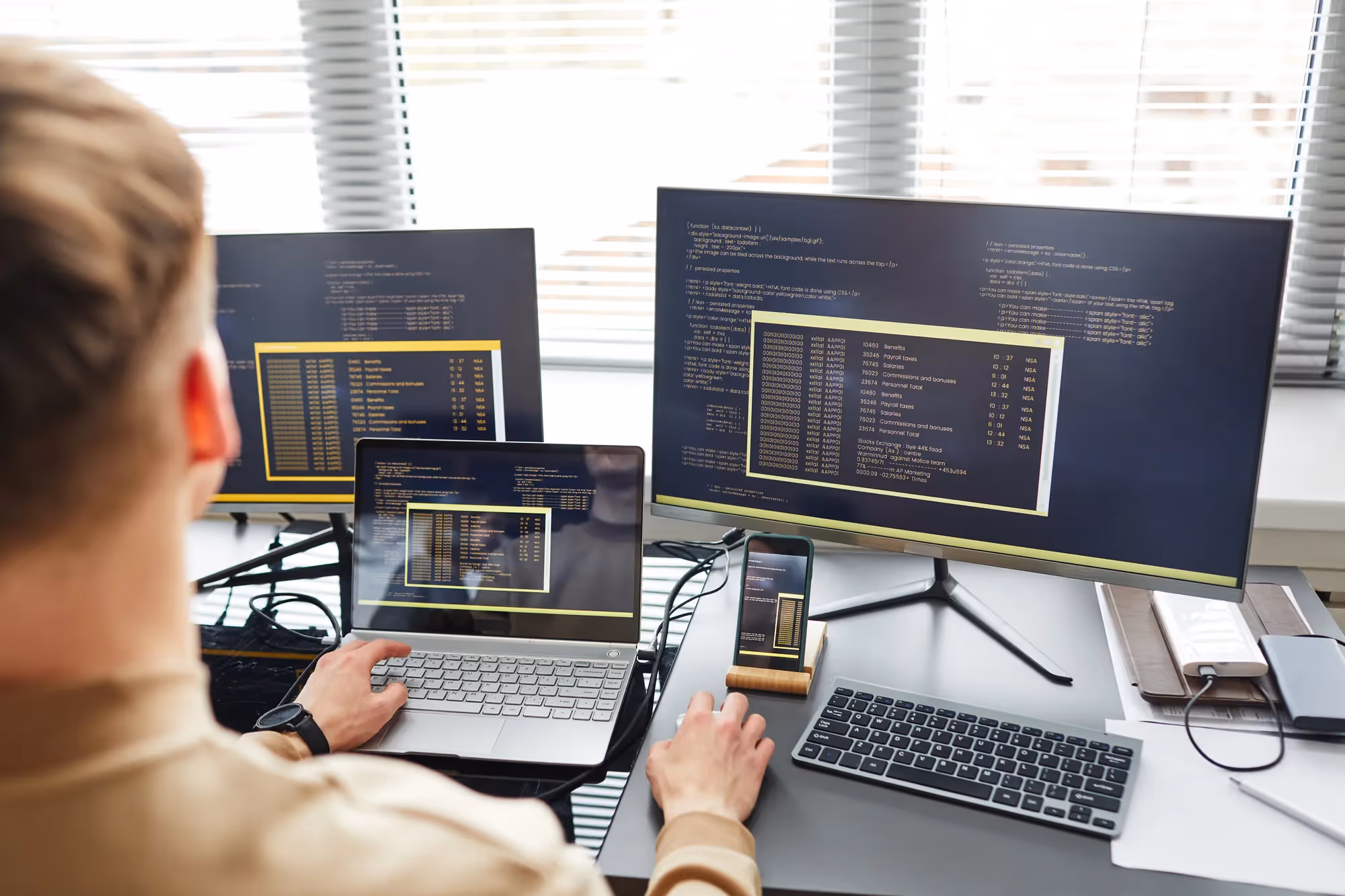 A man is working on a laptop with a monitor in front of him.