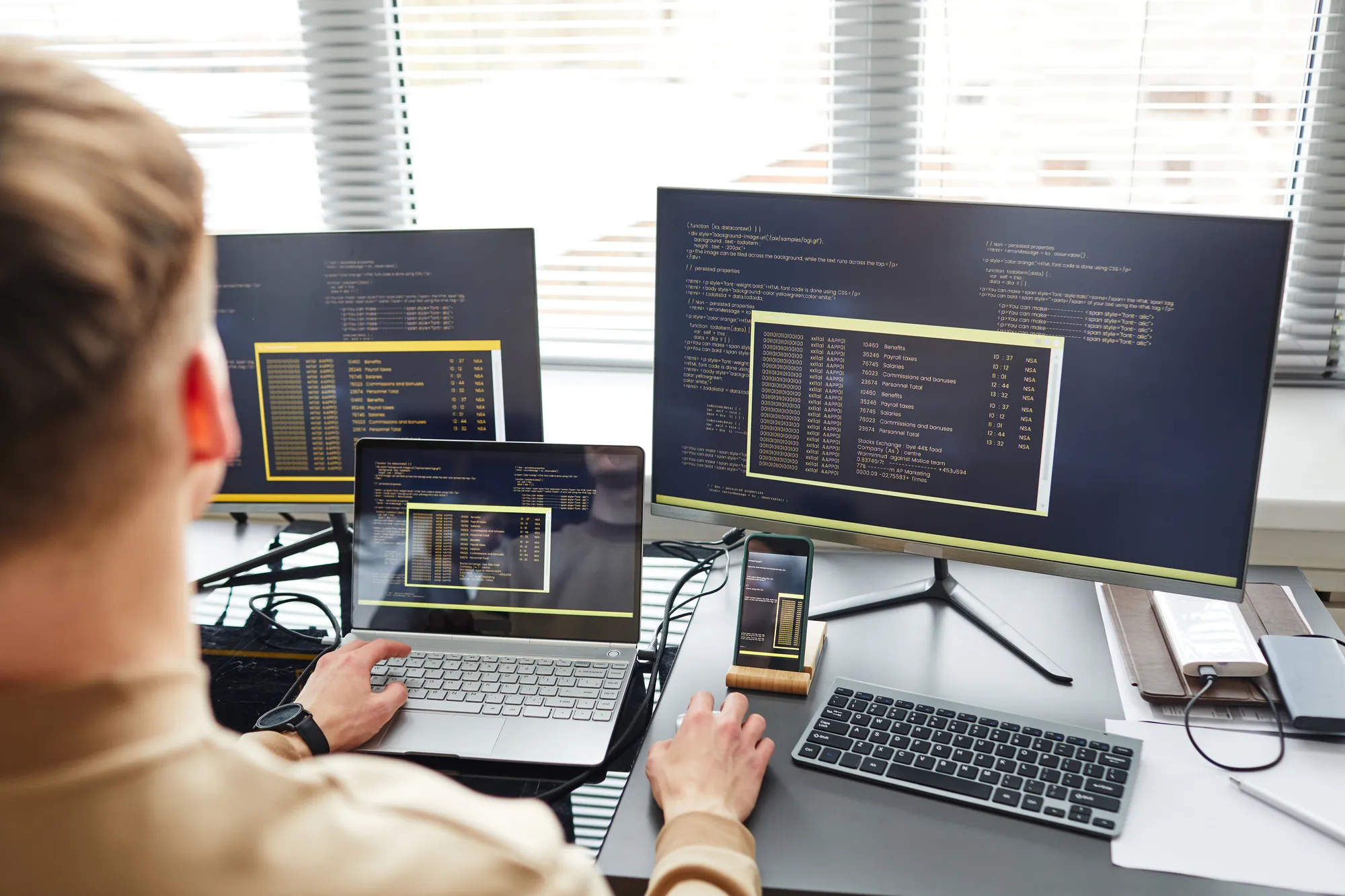 A man is working on a laptop with a monitor in front of him.