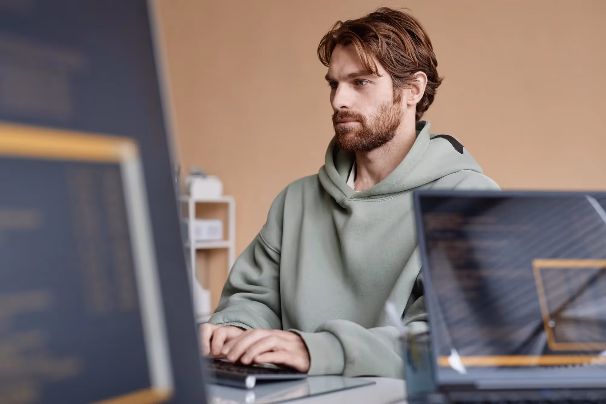 A man in a grey hoodie is typing on a laptop.