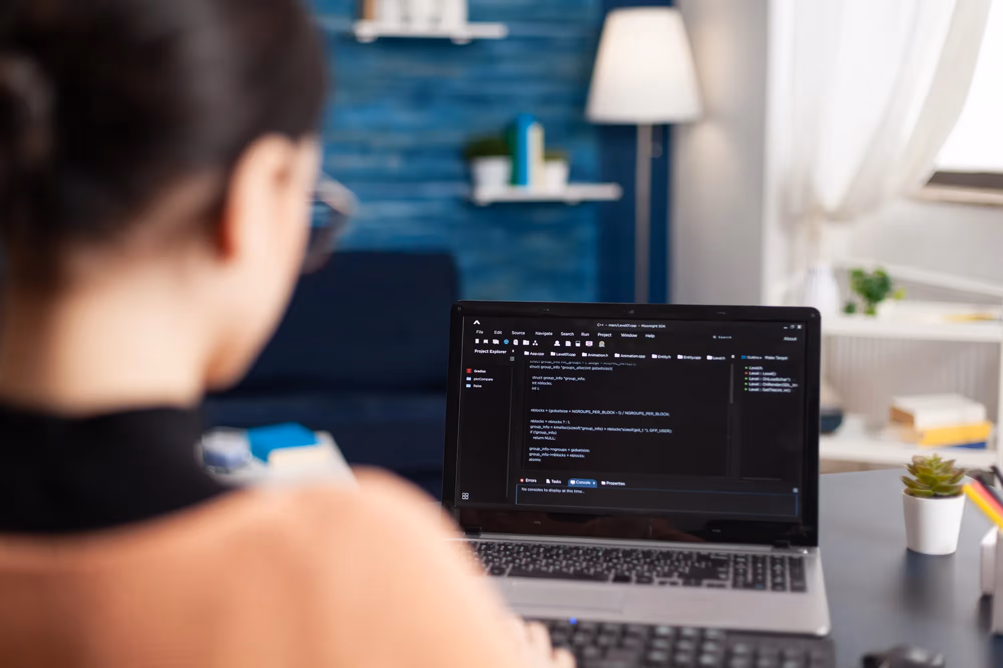 A woman is sitting in front of a laptop with a blue wall behind her.