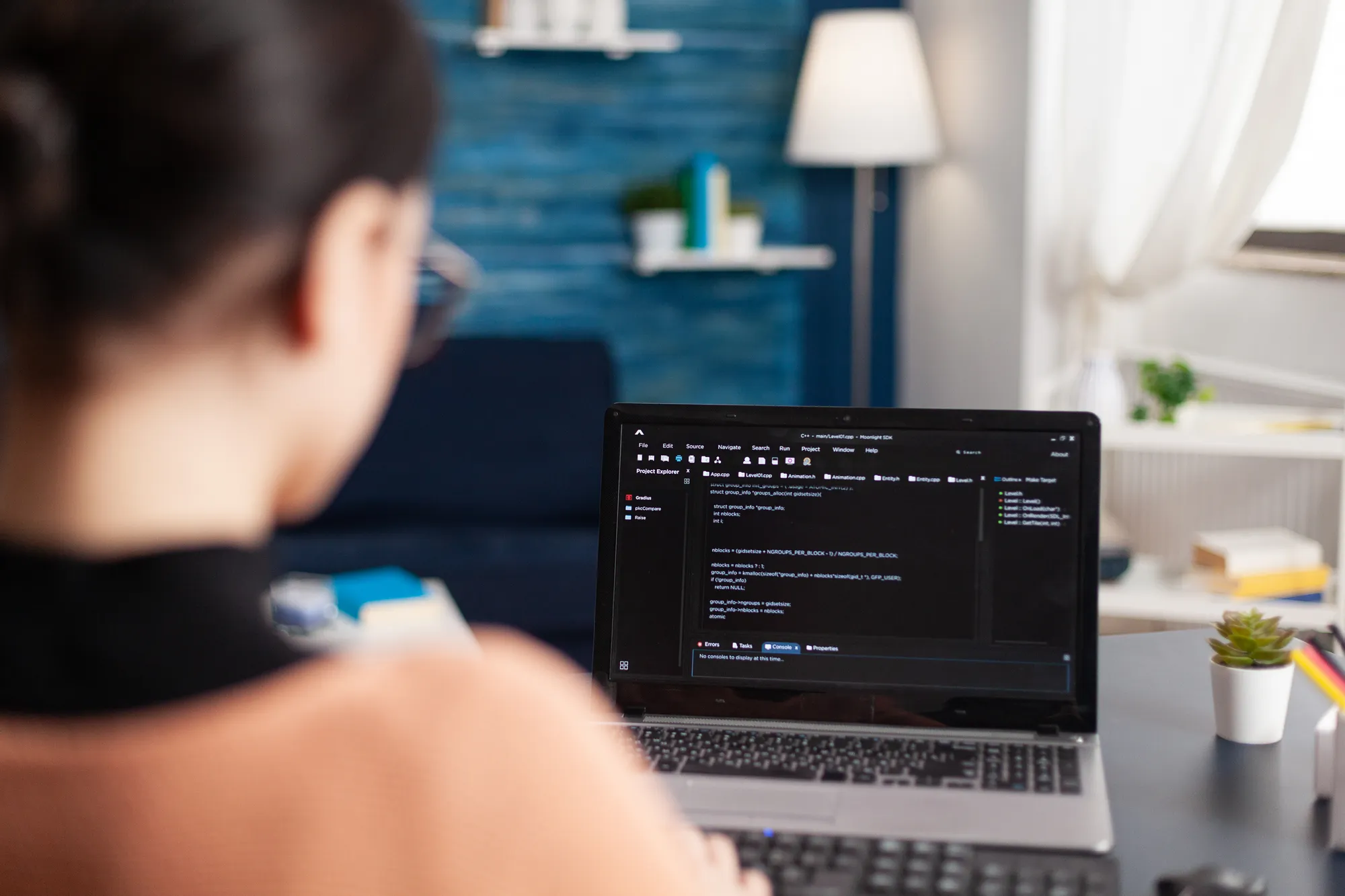 A woman is sitting in front of a laptop with a blue wall behind her.
