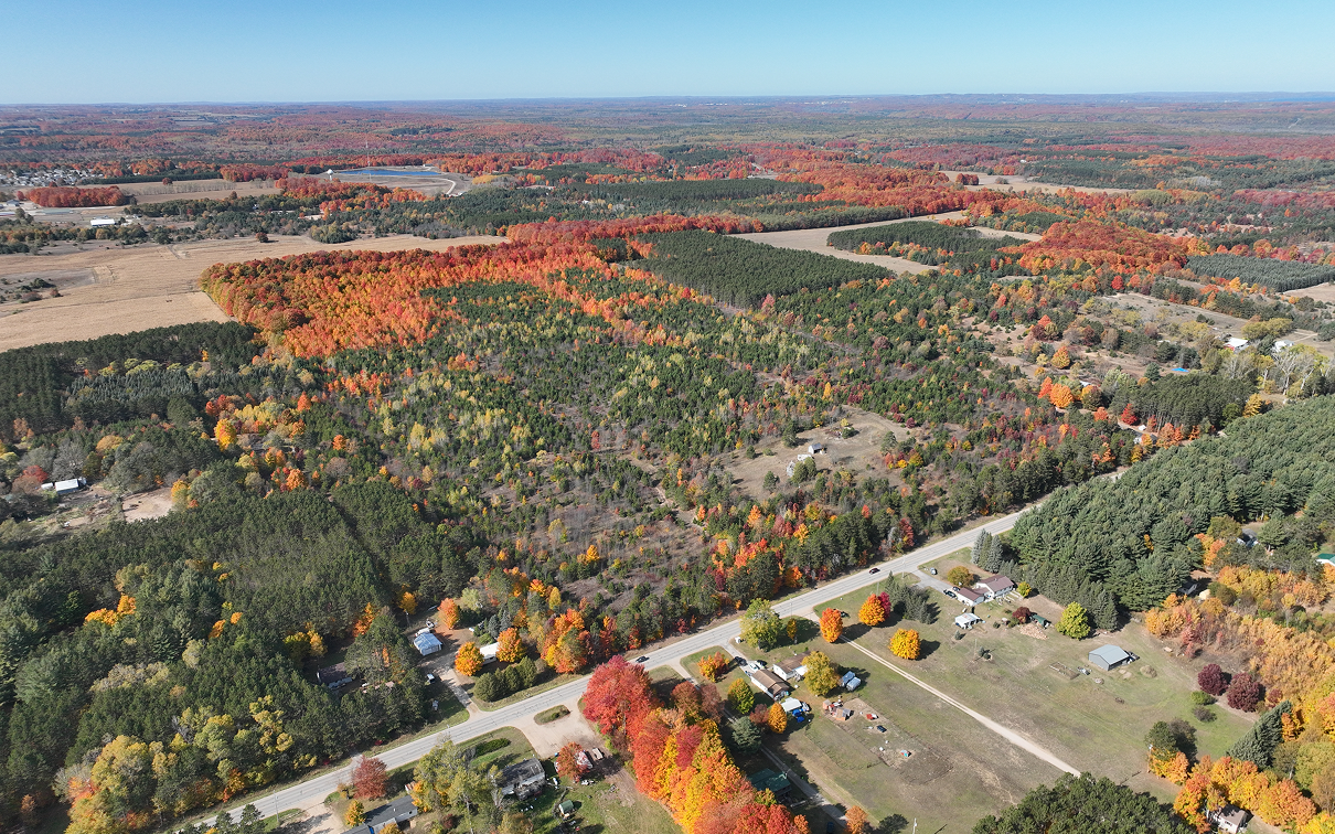 Aerial view of a rural landscape with autumn-colored forests and scattered homes.