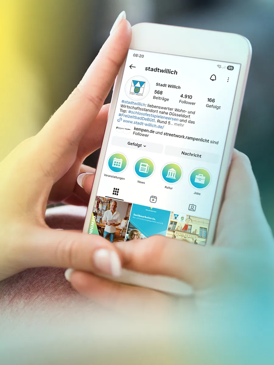 A smartphone with an Instagram profile from the city of Willich holds hands, shows contributions, followers and categories such as events, news, culture and jobs.
