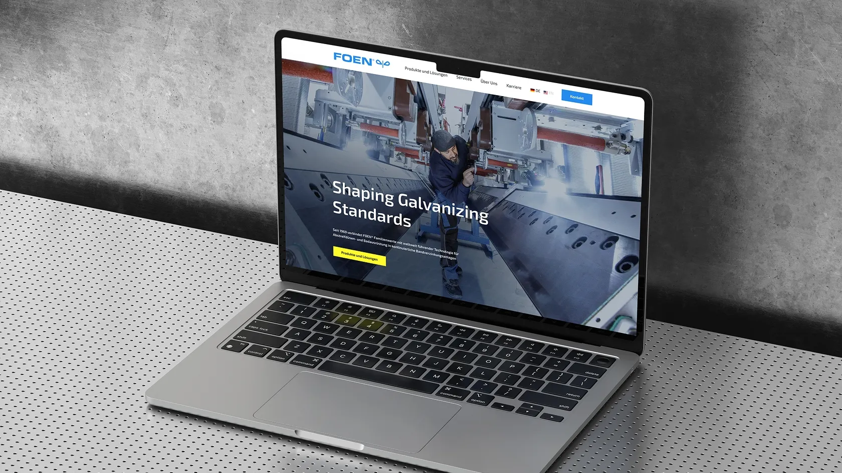 Laptop on perforated metal table shows FOEN's website with a picture of a technician at an electroplating plant.