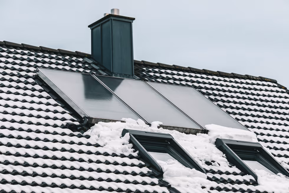 A snow covered roof with a solar panel on top.