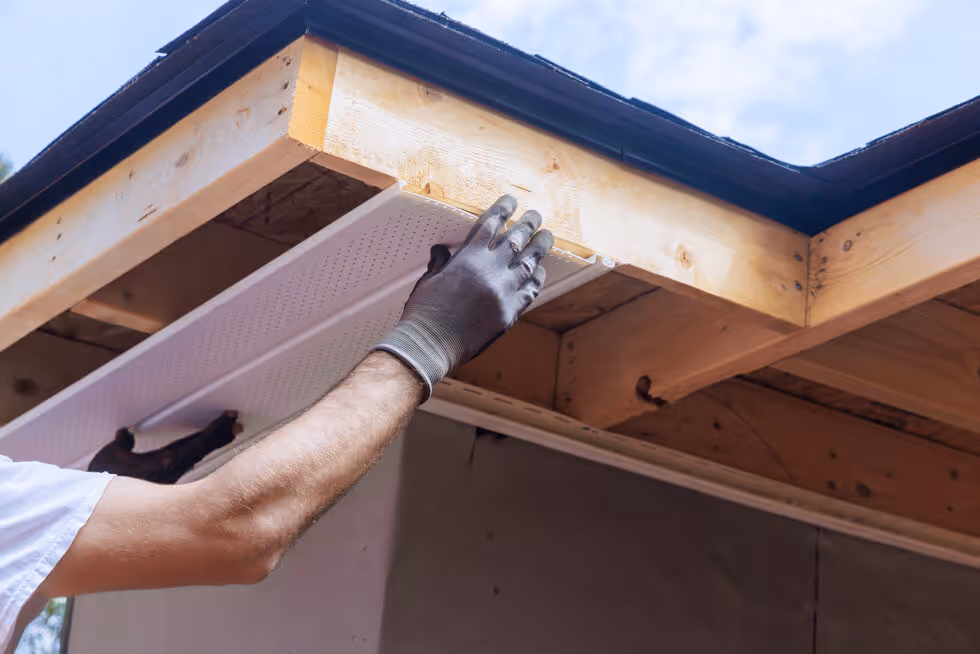 A man is working on a roof with a hammer and gloves.