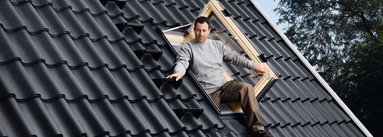 A man is standing on a roof with a window.