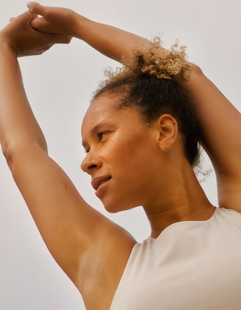 Close-up of a woman stretching her arms overhead, wearing a sleeveless top.